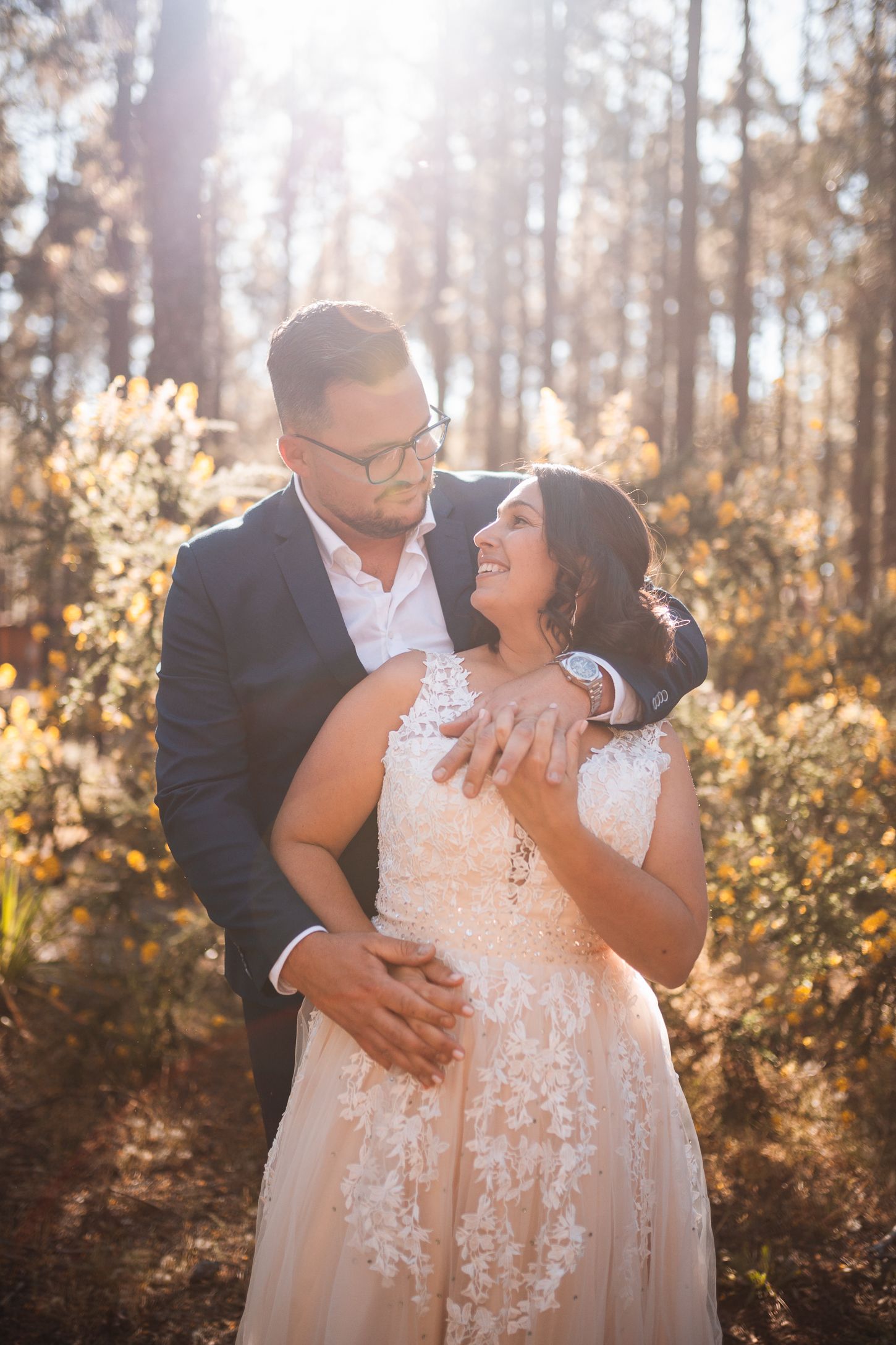 A tender embrace between newlyweds captured in golden forest light.