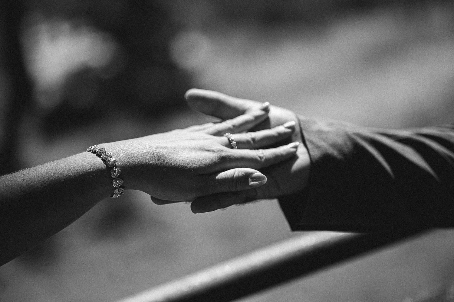 Black and white close-up of hands with engagement ring touching.