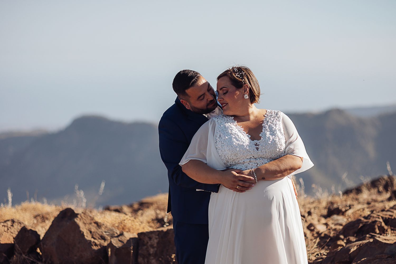 Couple in wedding attire sharing an intimate moment on a mountain overlook.