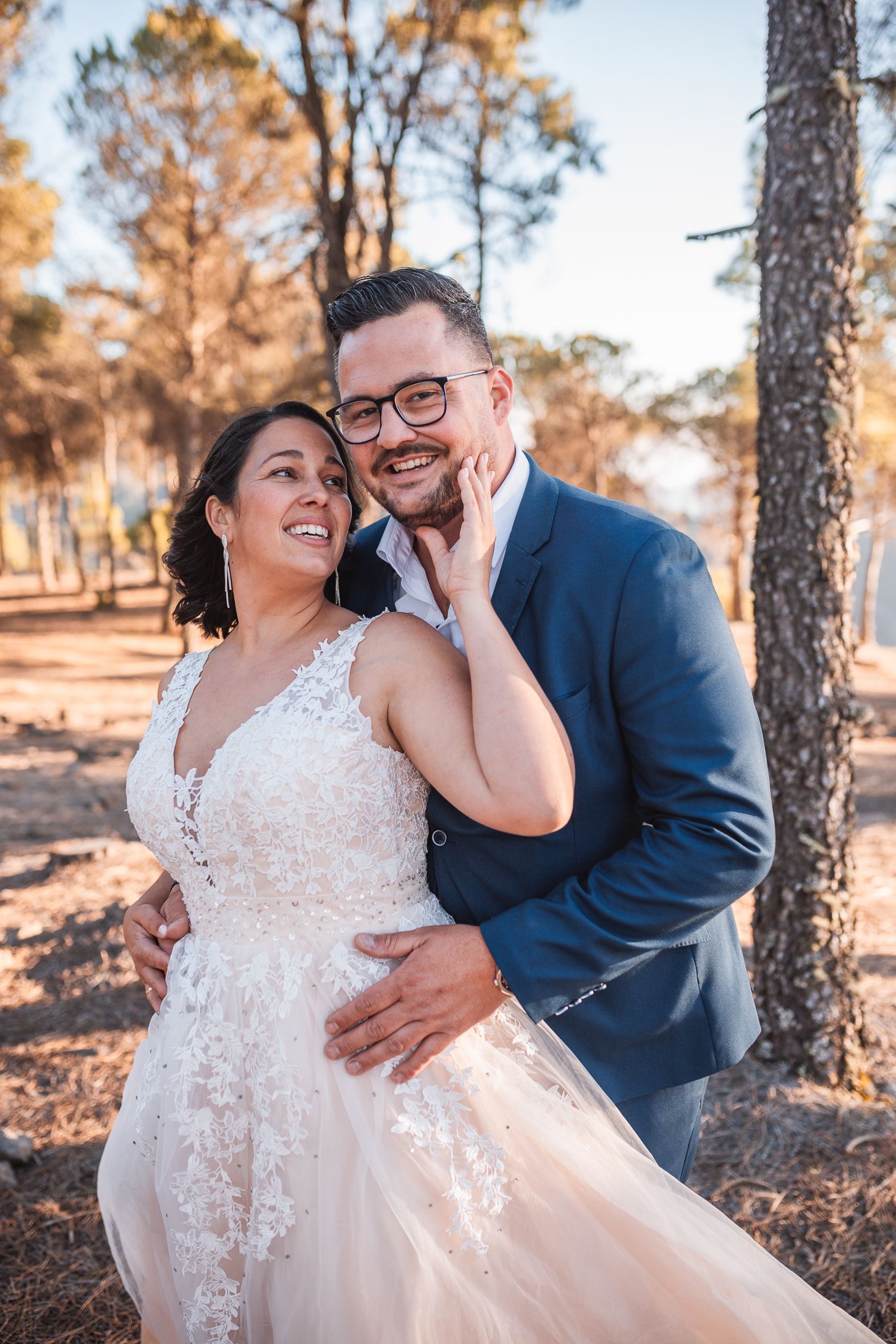 Joyful wedding portraits showing tender moments between newlyweds among pine trees at sunset.