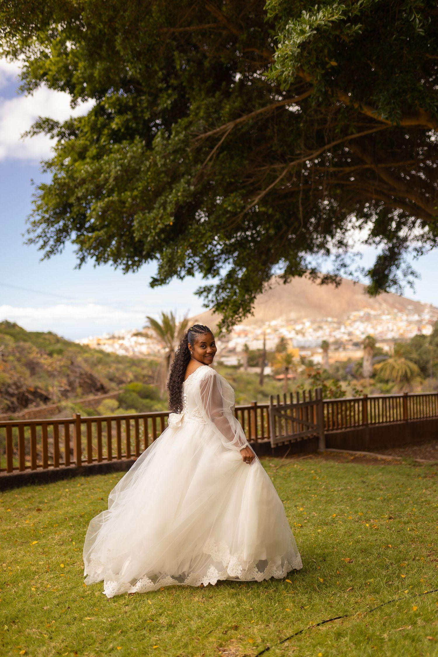 Bride in flowing white dress poses on grassy hillside during outdoor wedding photoshoot.