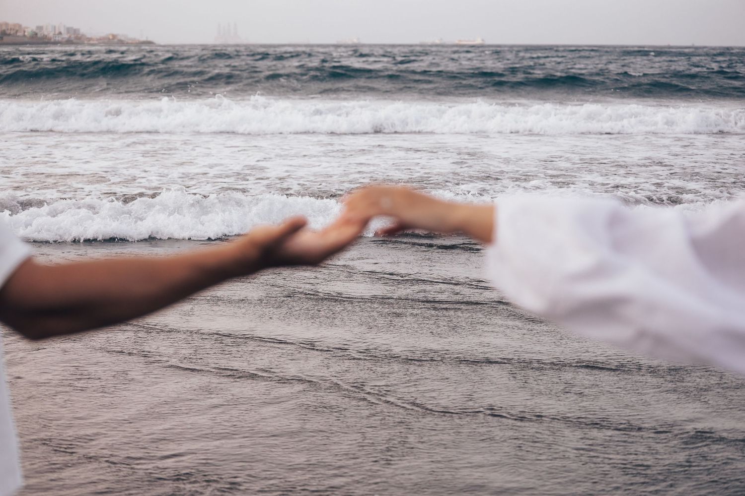 Hands reaching out to touch each other against an ocean backdrop.