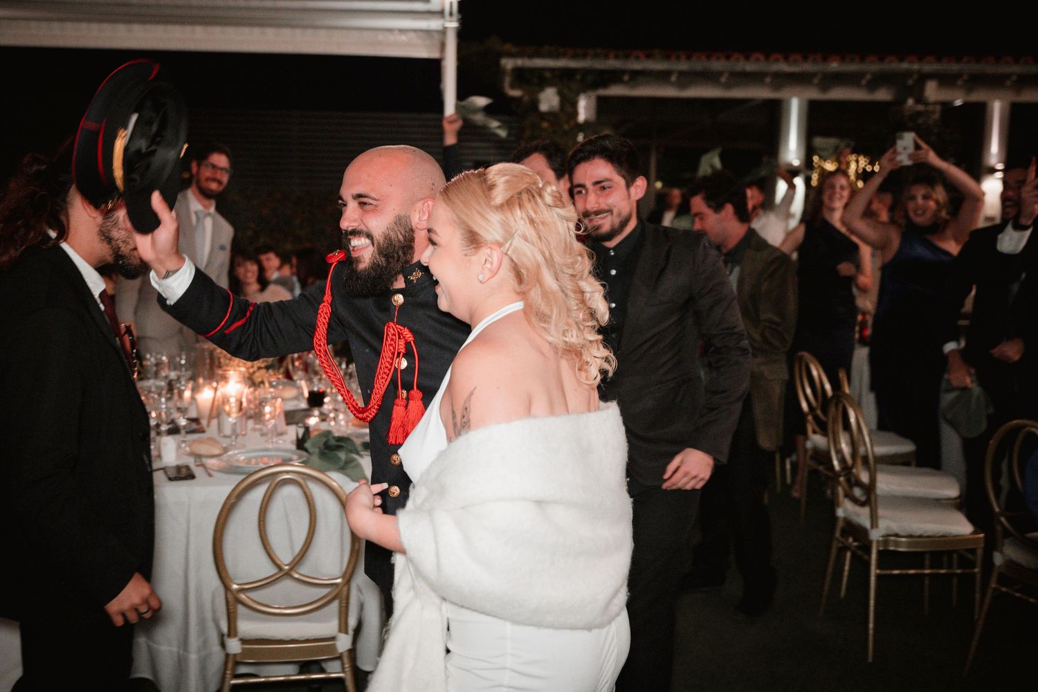 Wedding reception celebration with guests standing and cheering at decorated tables.