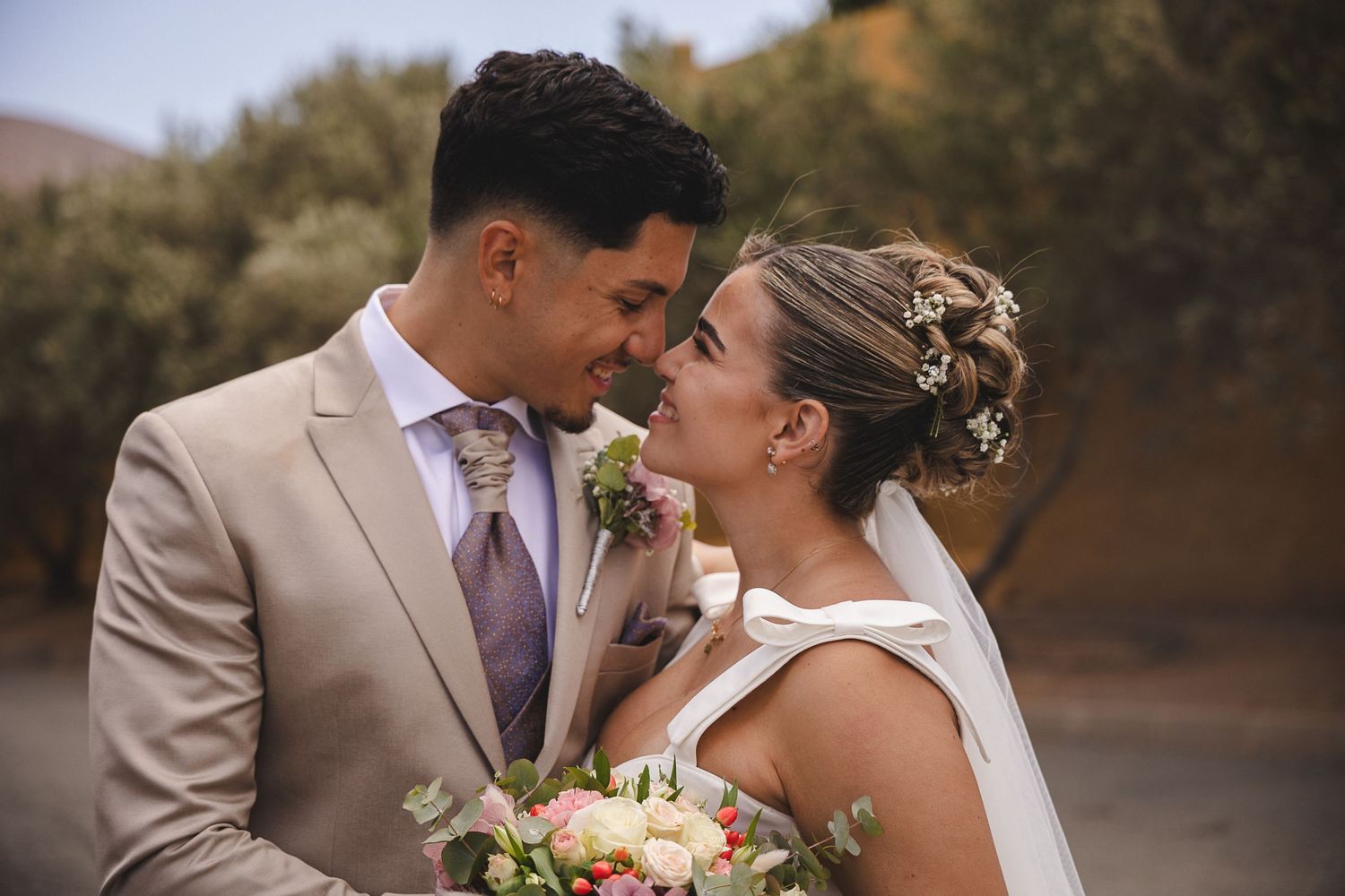 A romantic wedding moment captured between a couple in tan and white attire.