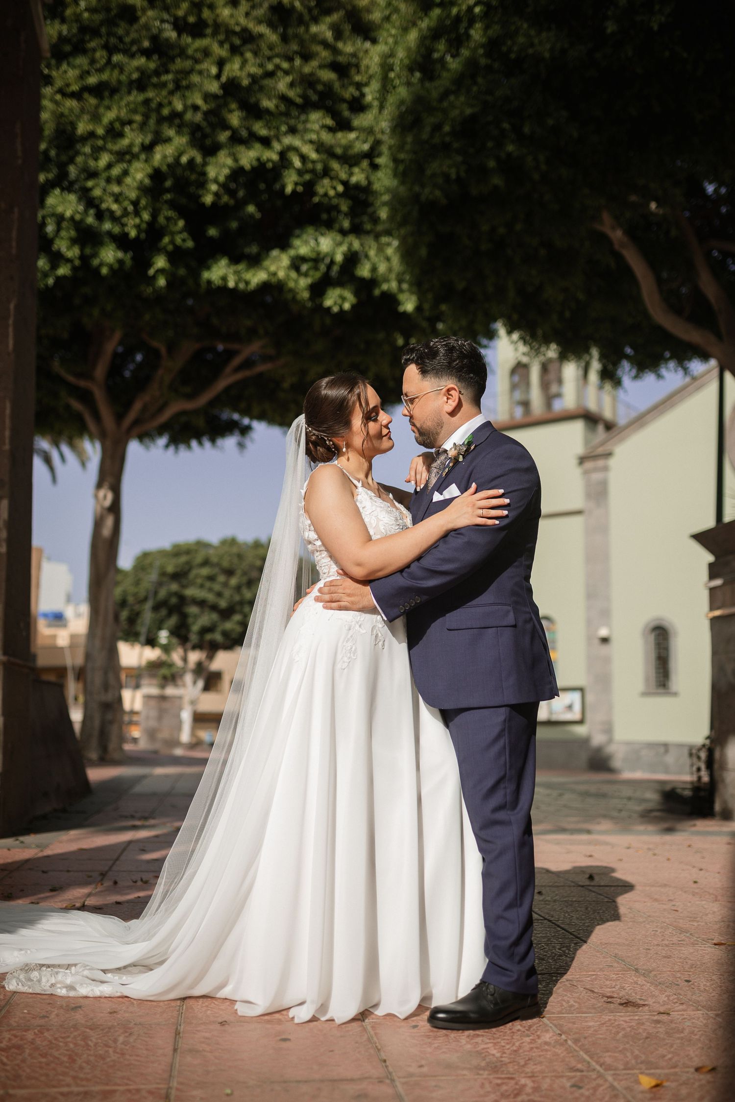 A couple shares a romantic moment on their wedding day on a tree-lined street.