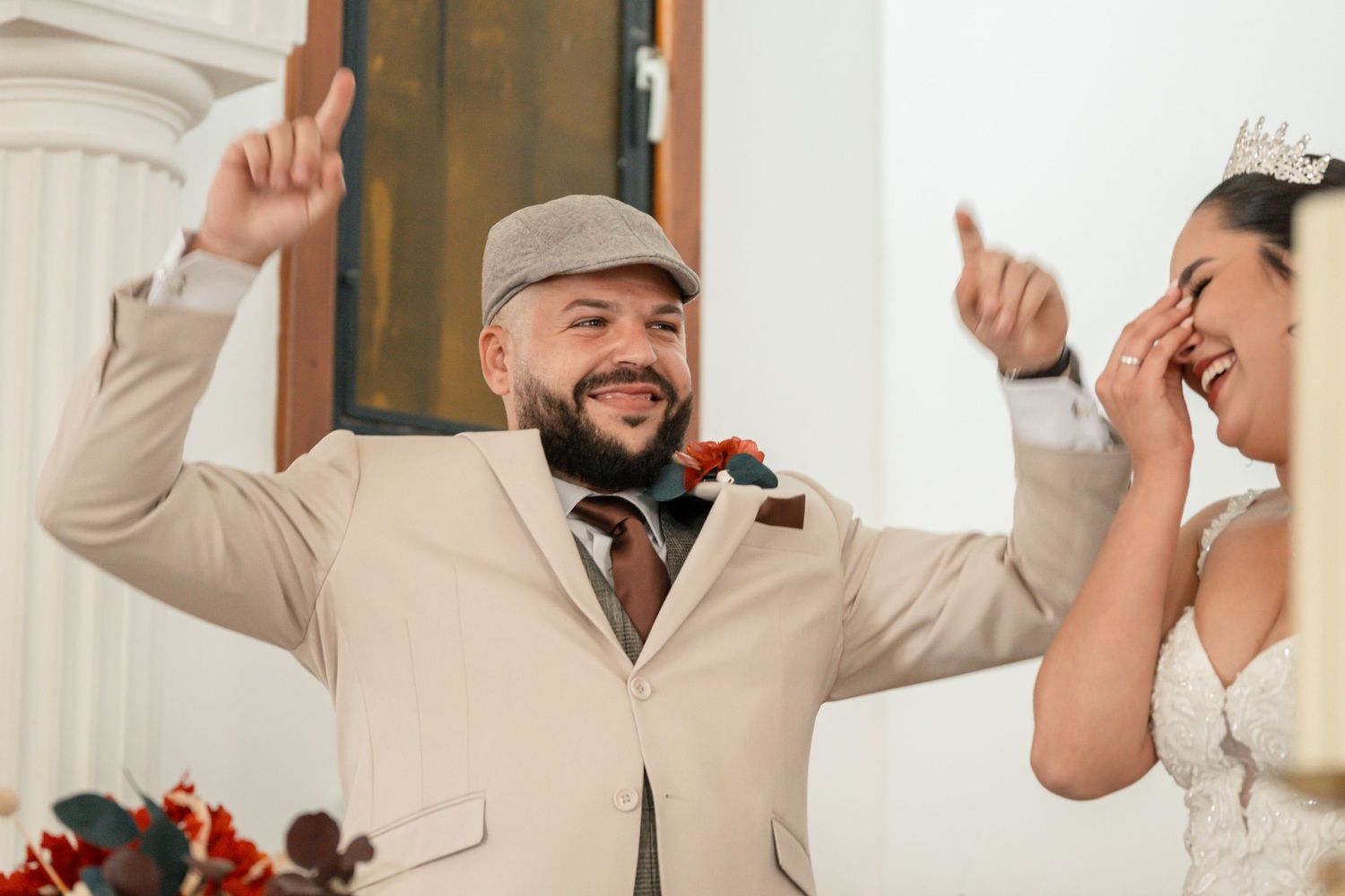Groomsmen celebrate joyfully in matching tan suits and caps at an outdoor wedding.