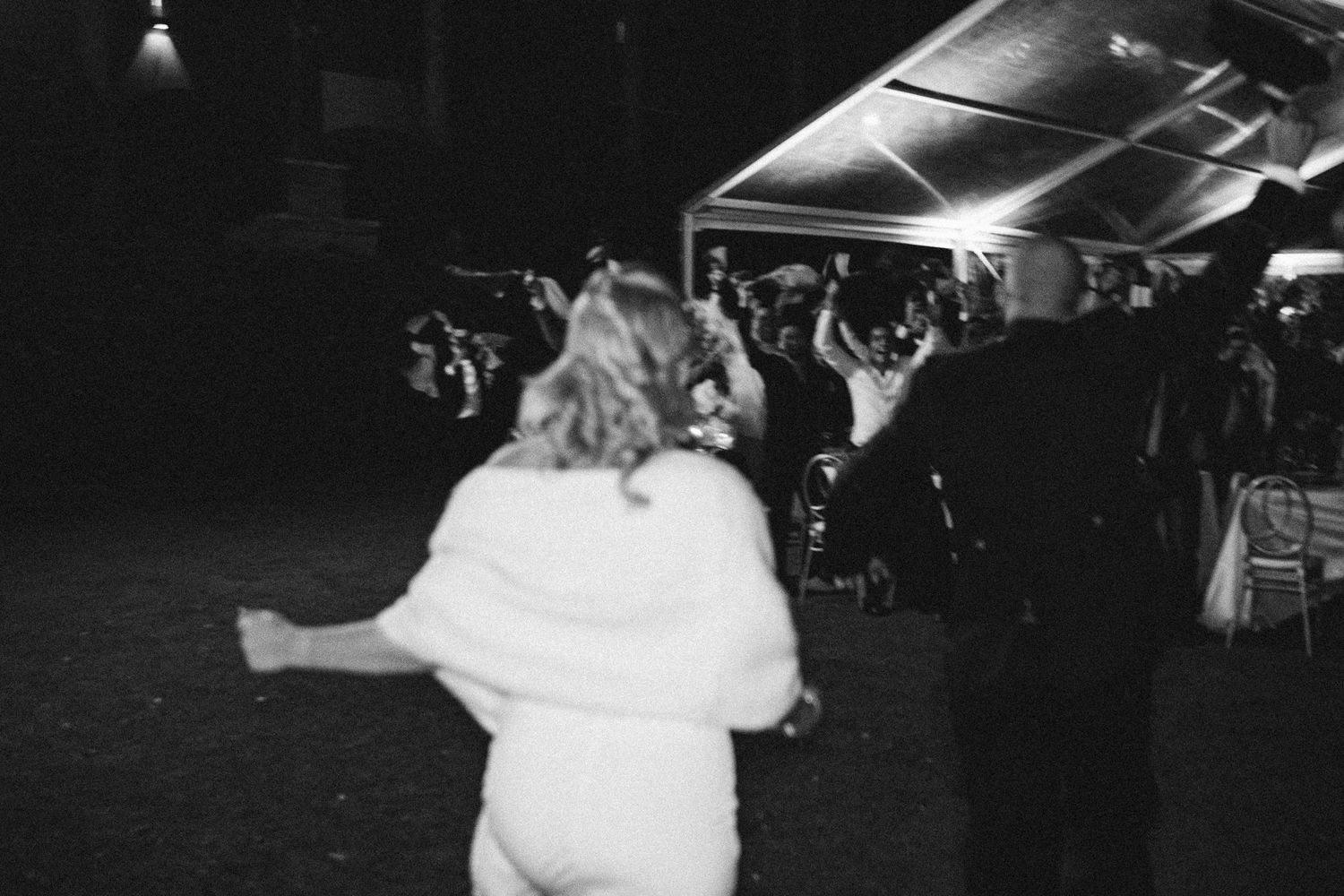 Black and white photo of a couple dancing at a wedding reception under a tent.