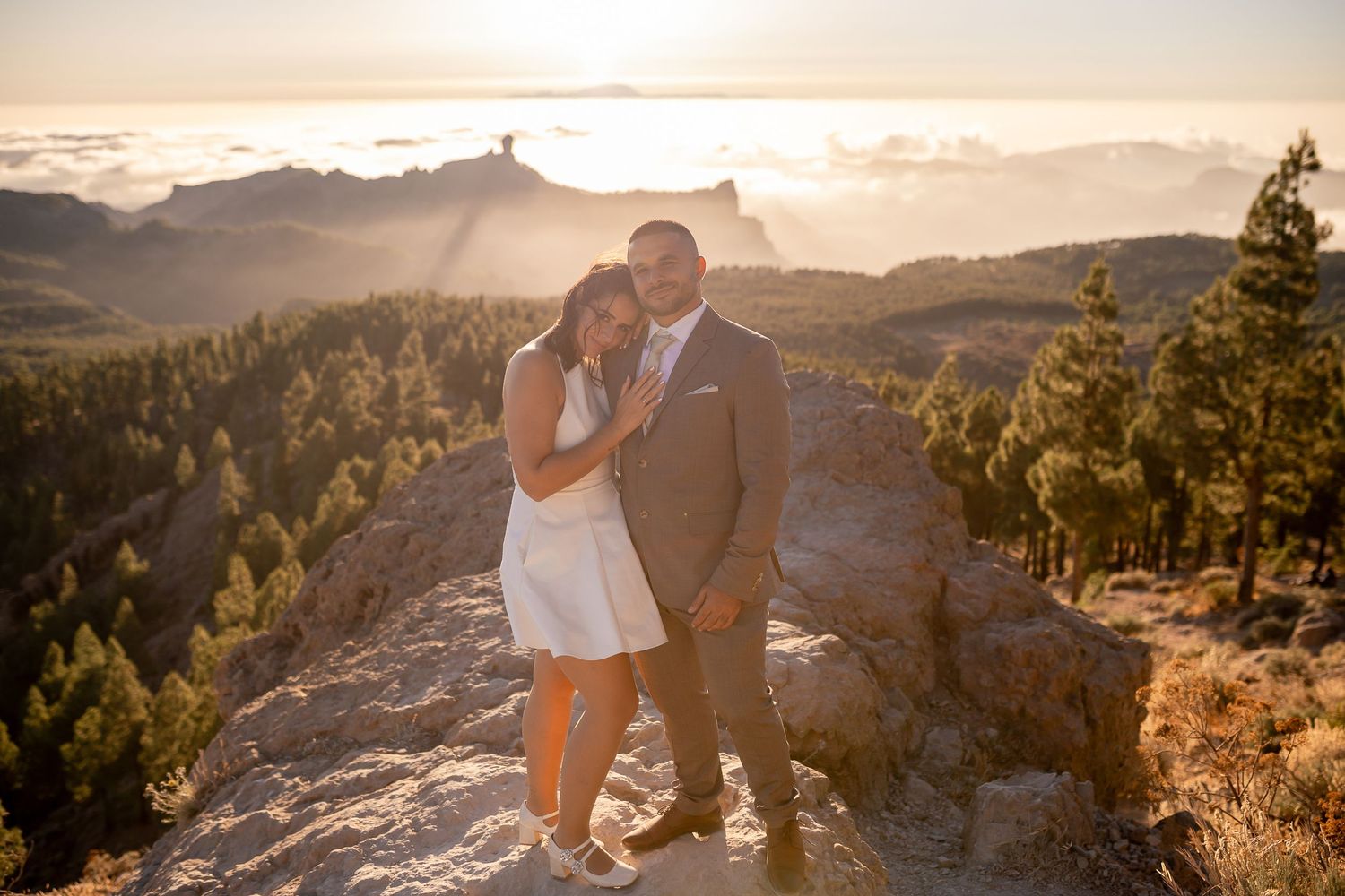 A couple enjoys a romantic moment on a mountain overlook during sunset.