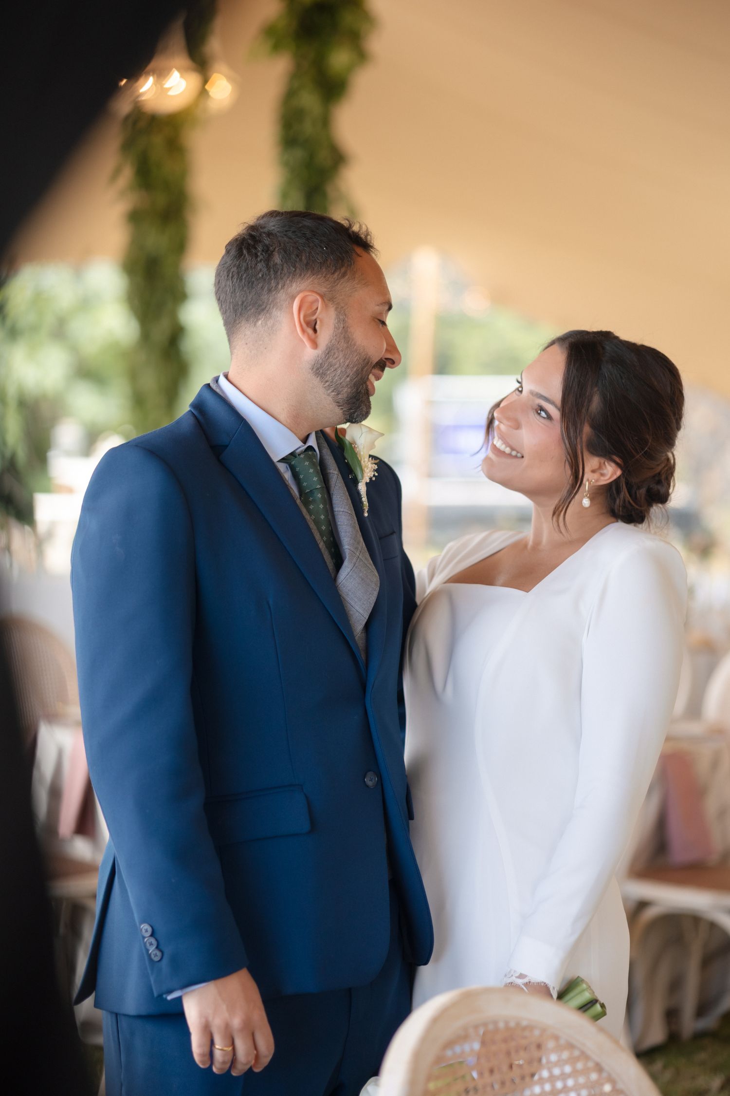 A smiling bride in a white gown and groom in a navy suit share a tender moment at their wedding reception.