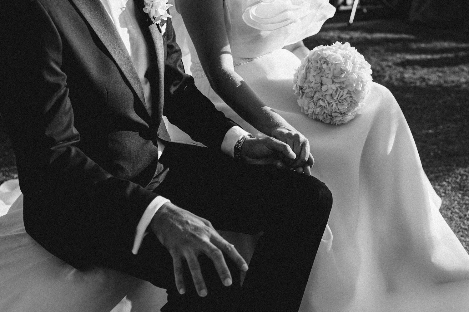 Black and white wedding detail photo showing hands holding during an intimate ceremony moment.