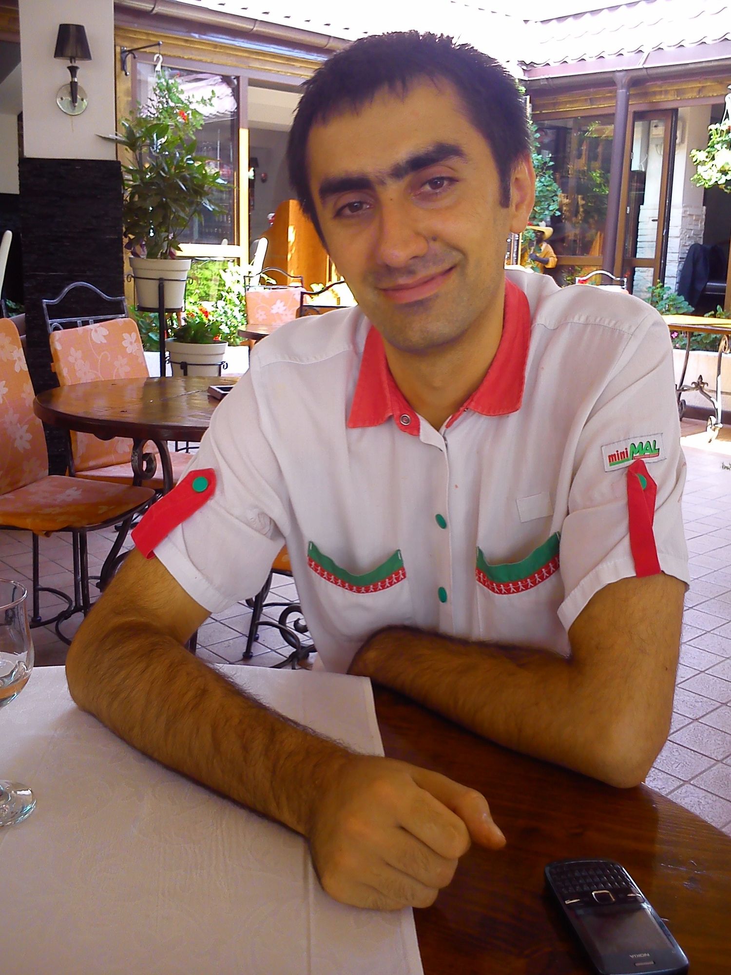 Someone sitting at an outdoor patio table wearing a white polo shirt.