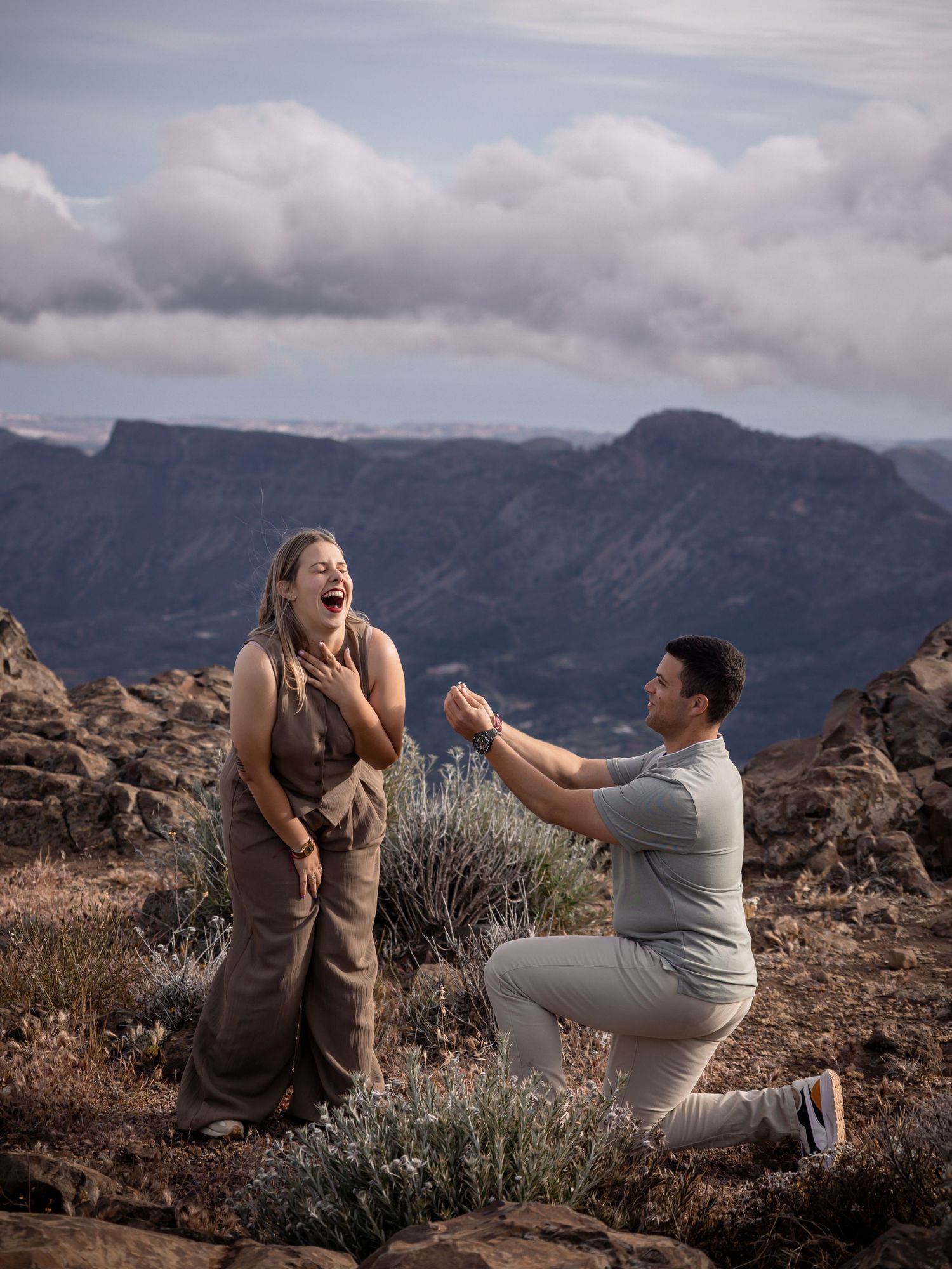 Surprise proposal moment captured on rocky mountain terrain with dramatic backdrop.