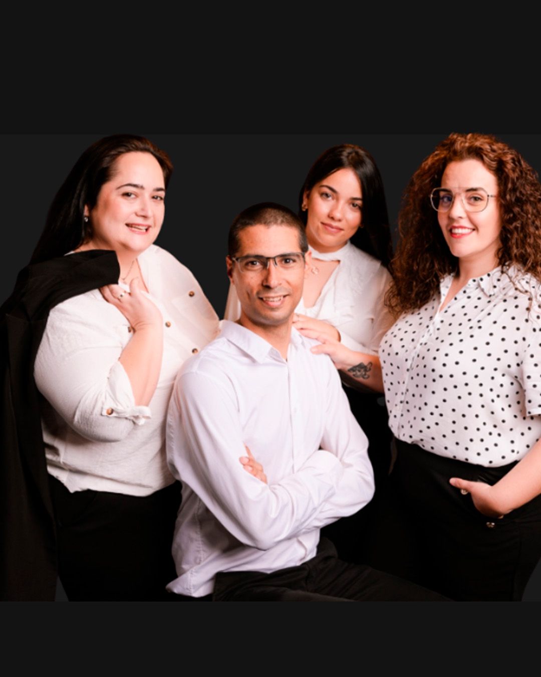 Professional studio portrait of four people wearing white and polka dot tops against a dark background.