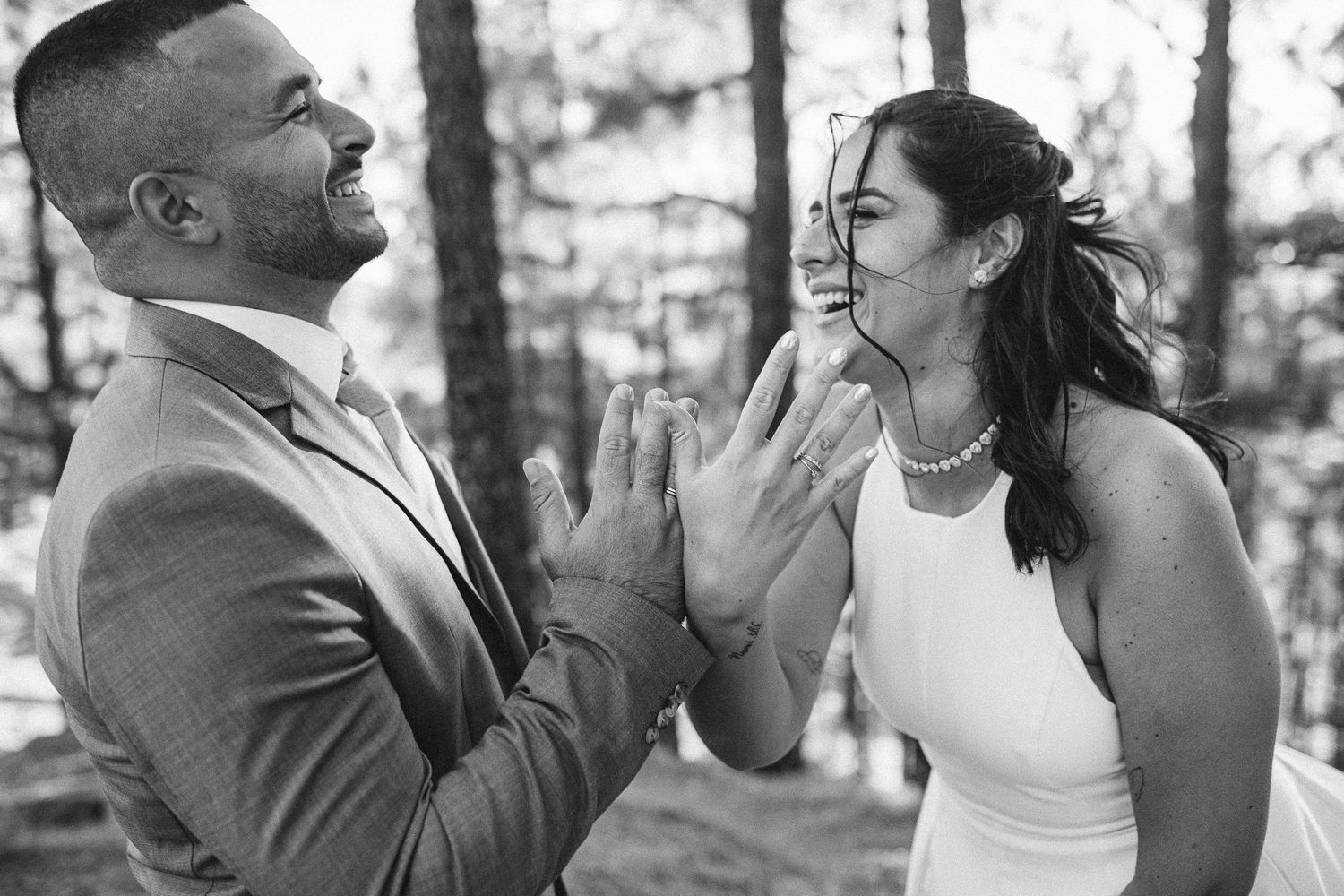 A couple shares joyful laughter during their outdoor wedding photo session in a forest setting.