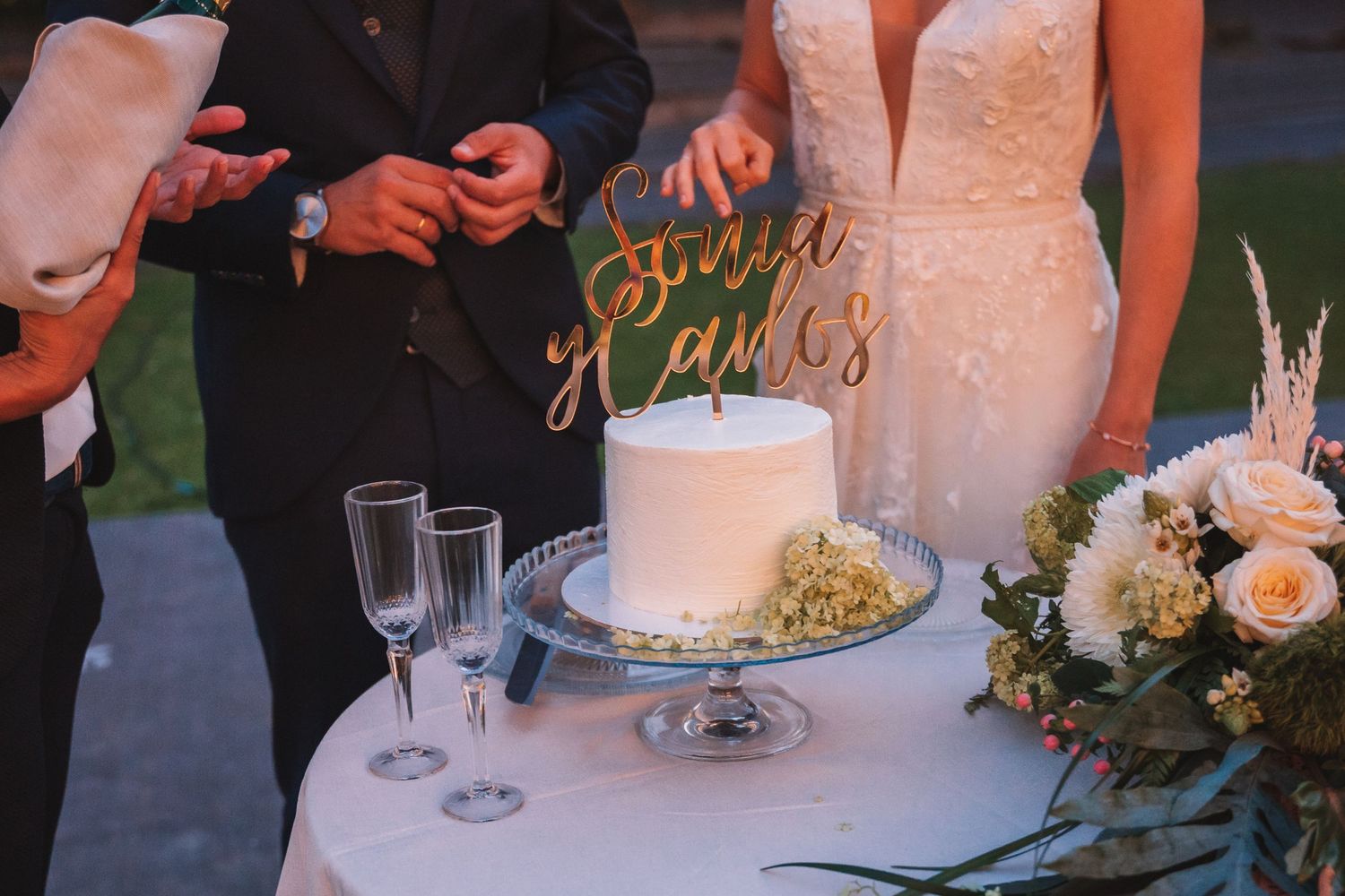 Wedding reception details with white cake and decorative table settings at dusk.