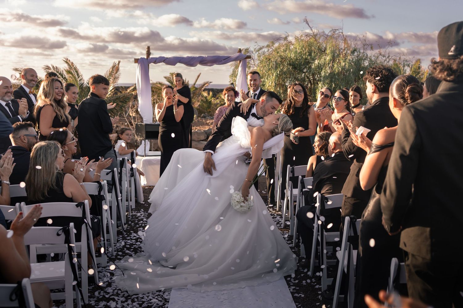 A dramatic wedding ceremony exit with confetti and guests cheering in an outdoor setting.
