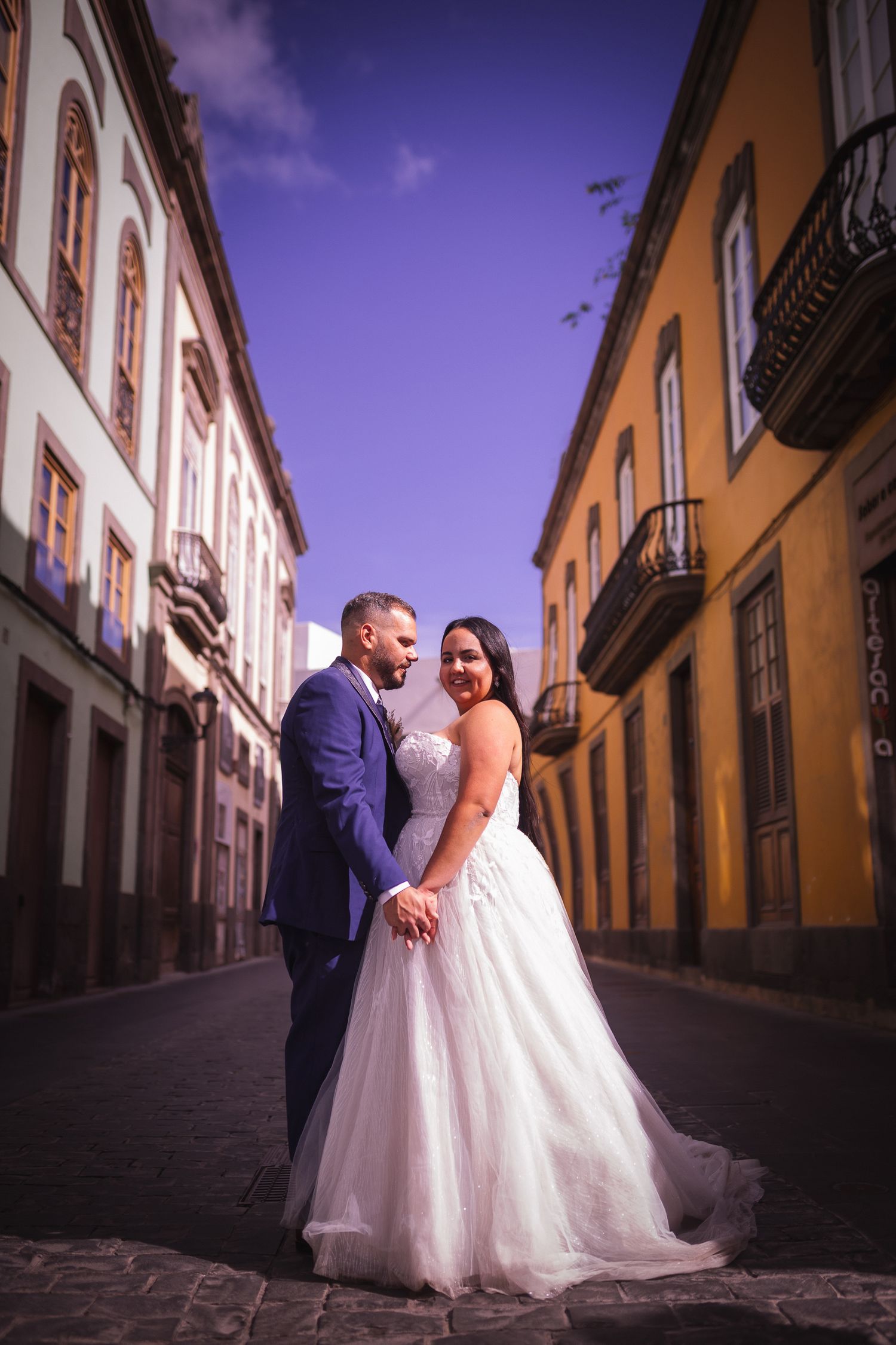 Romantic wedding photo on a cobblestone street with purple sky and historic architecture.