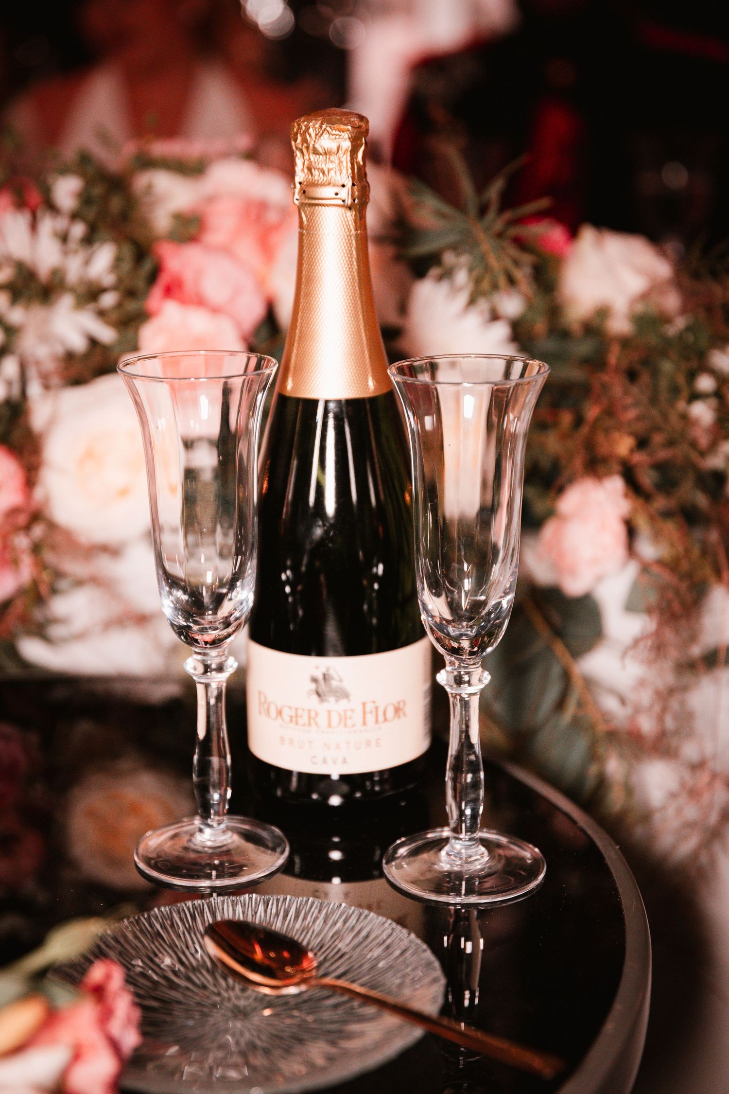 Champagne bottle and two empty flutes displayed with pink floral decorations.