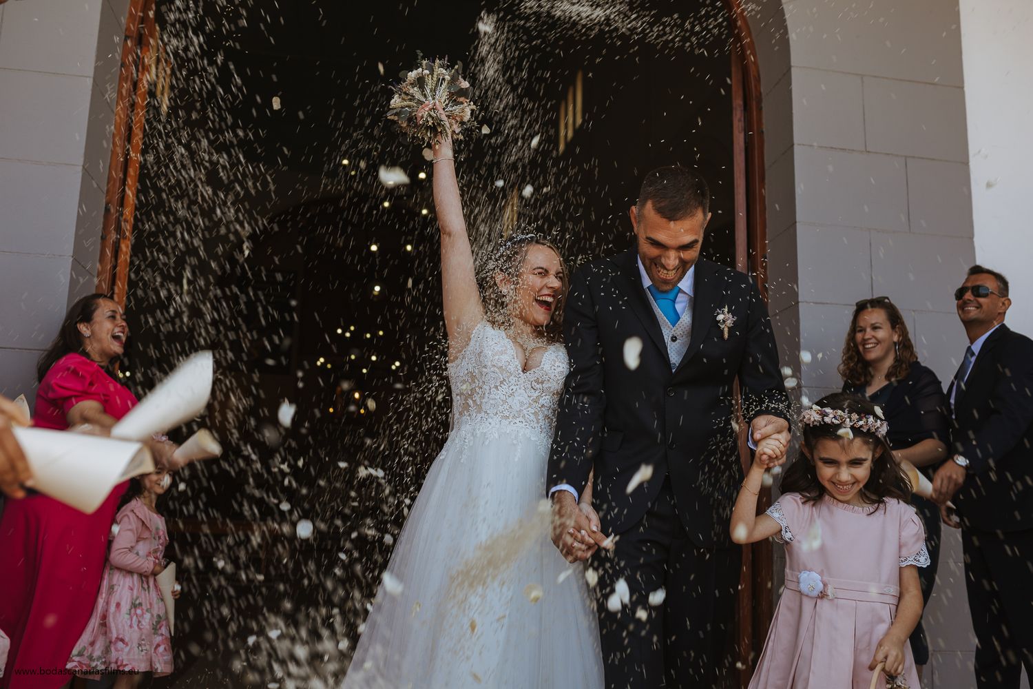 Wedding party celebration with guests throwing rice outside church entrance.