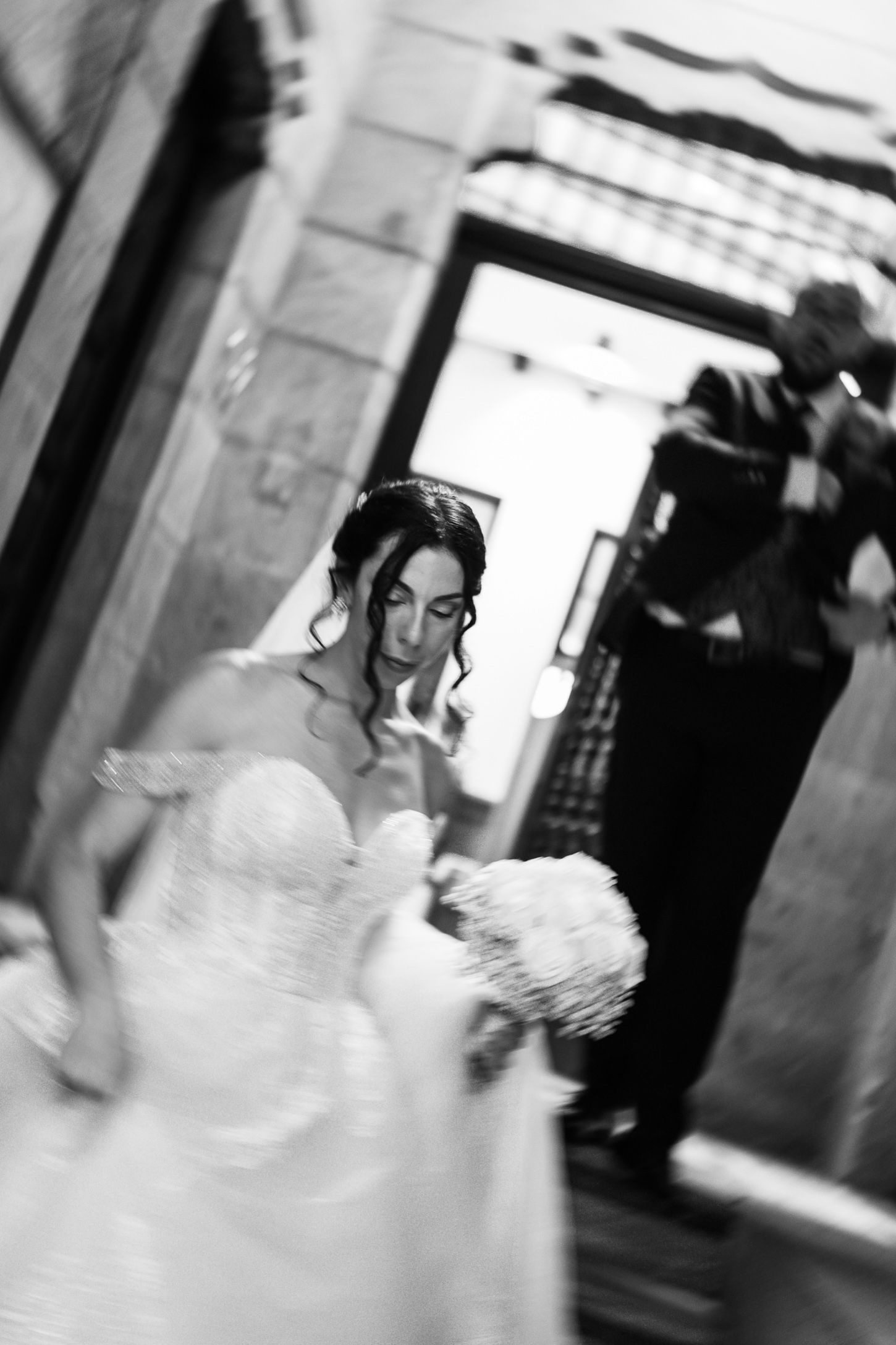 Artistic black and white motion blur captures movement of a bride in a wedding gown.