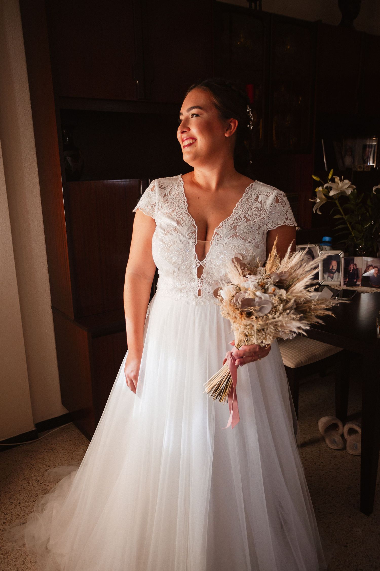 A beautiful white wedding dress with lace details and a flowing tulle skirt displayed in a dimly lit room.