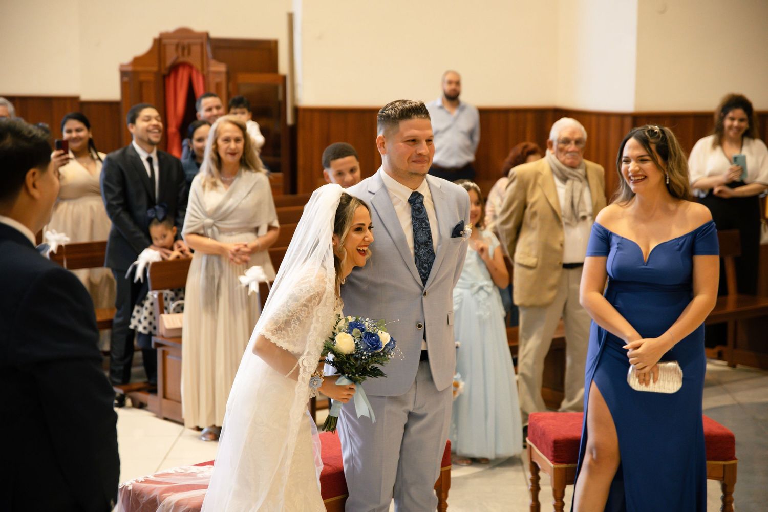 Bride and groom walking down church aisle during wedding ceremony with guests and bridesmaid in blue dress smiling.