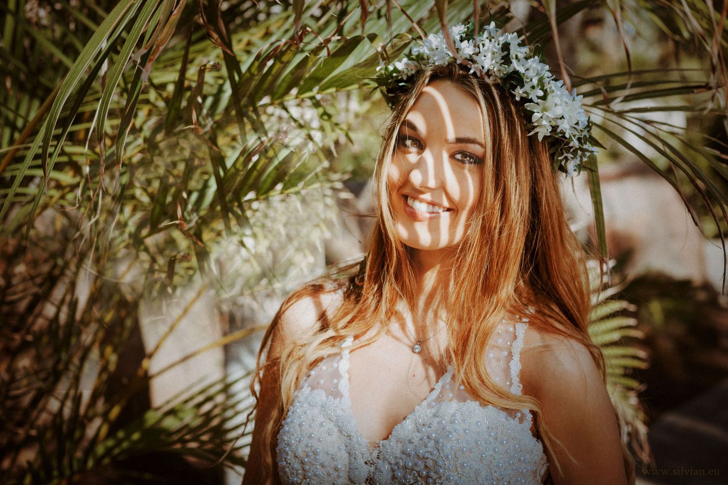 A bride poses in natural sunlight filtered through tropical palm fronds.