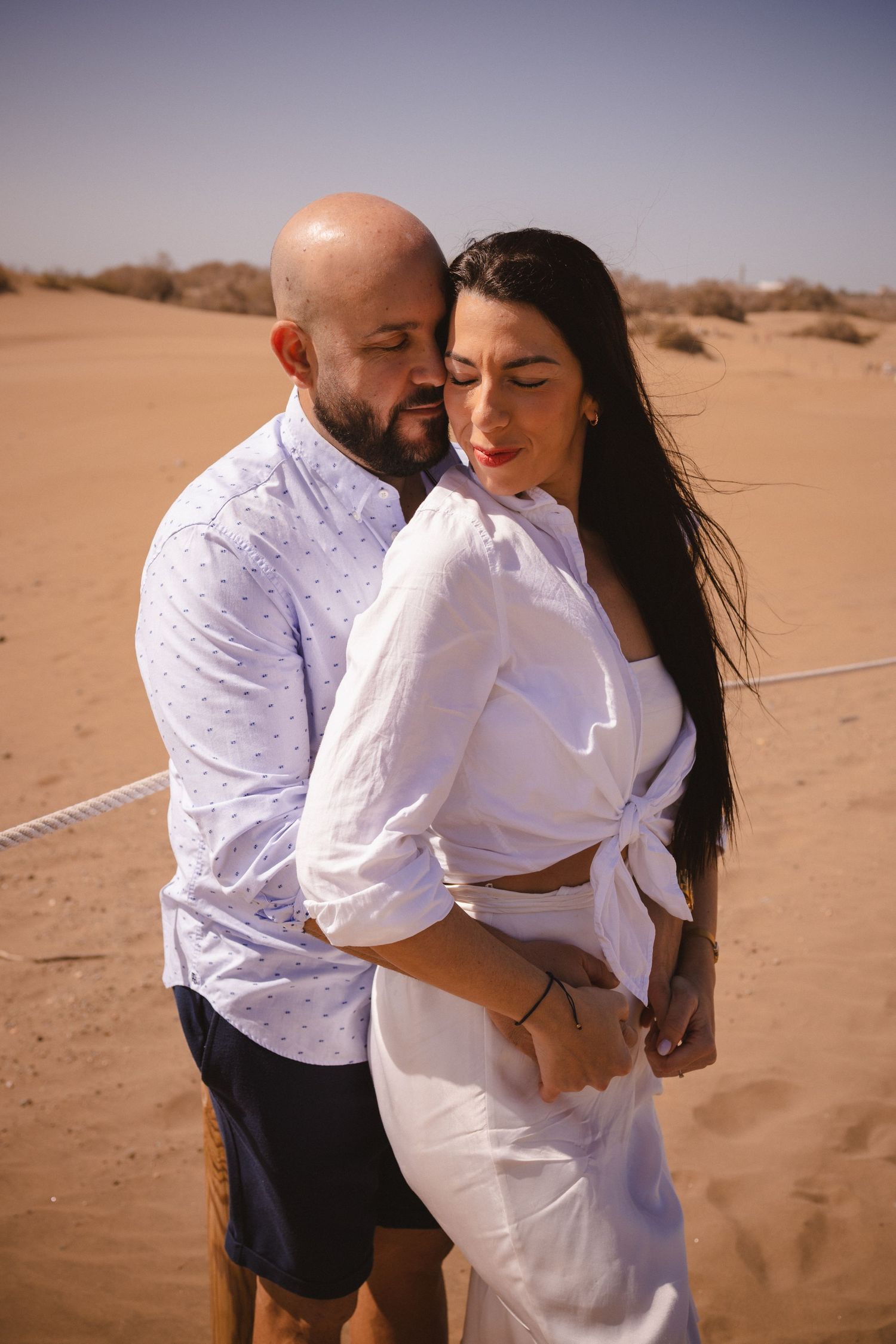 Romantic couple in white clothing embracing on desert sand dunes.