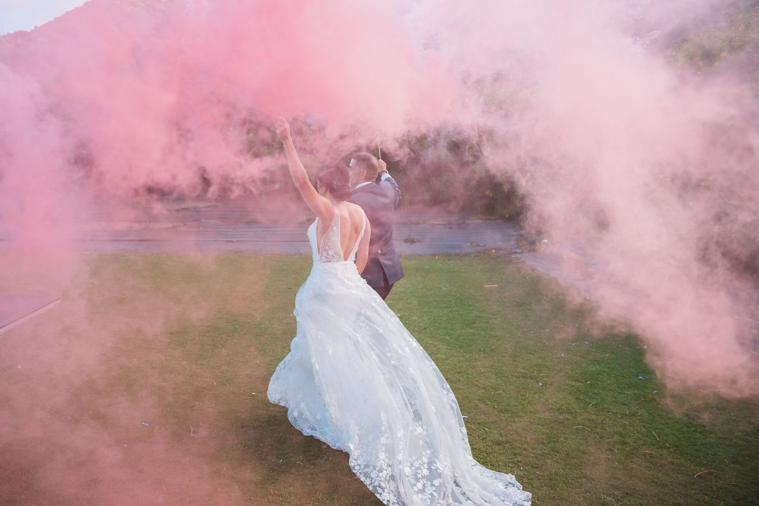 Pink smoke creates a dreamy atmosphere around a wedding couple in an outdoor setting.