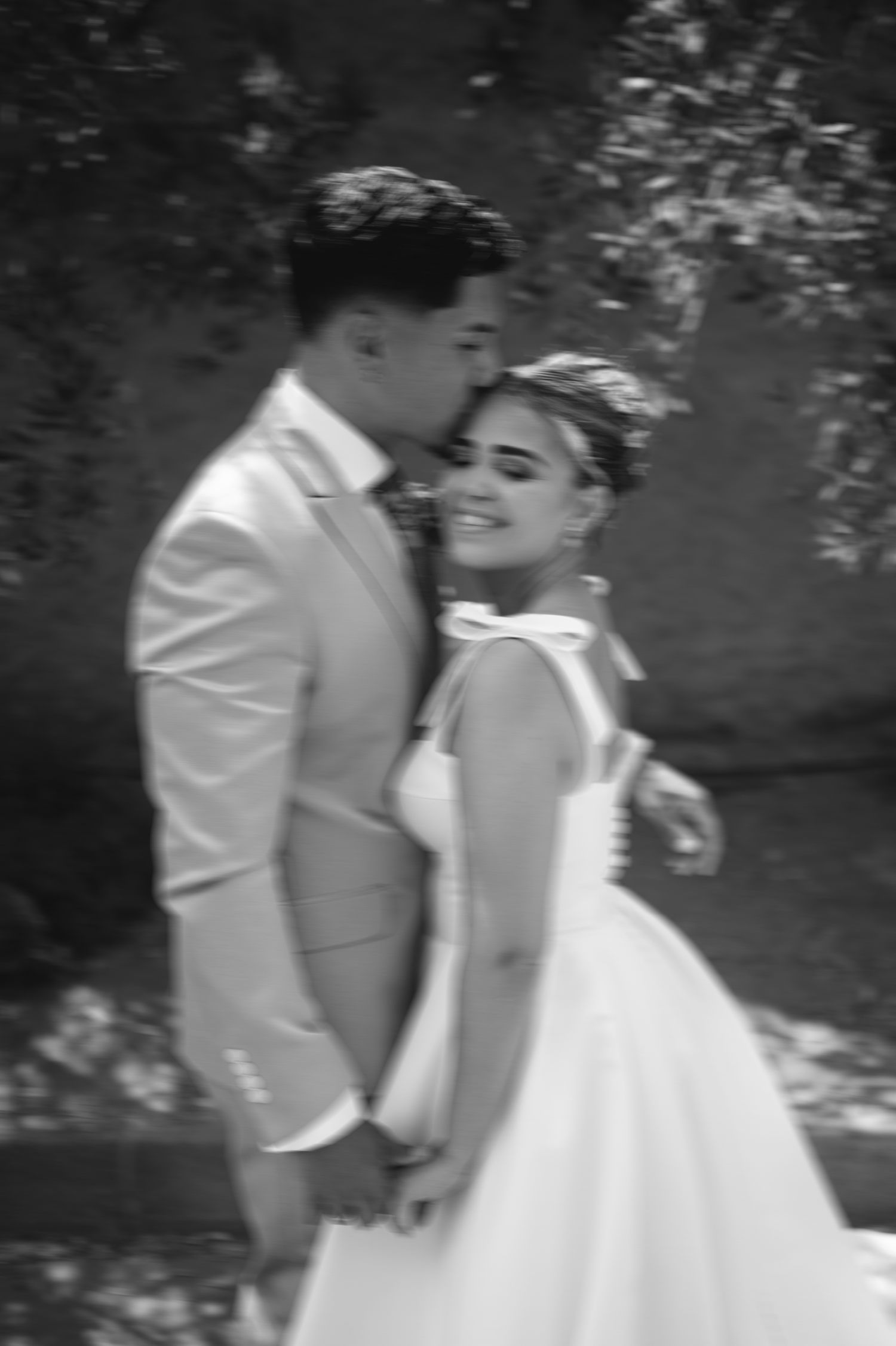 A black and white portrait of a couple in wedding attire sharing an intimate moment.