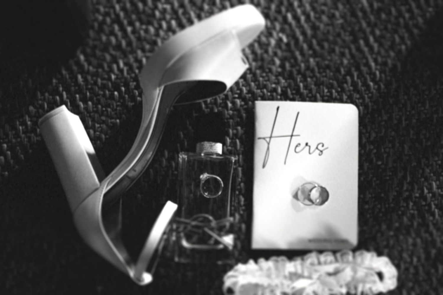 Wedding details and rings photographed on black leather surface.