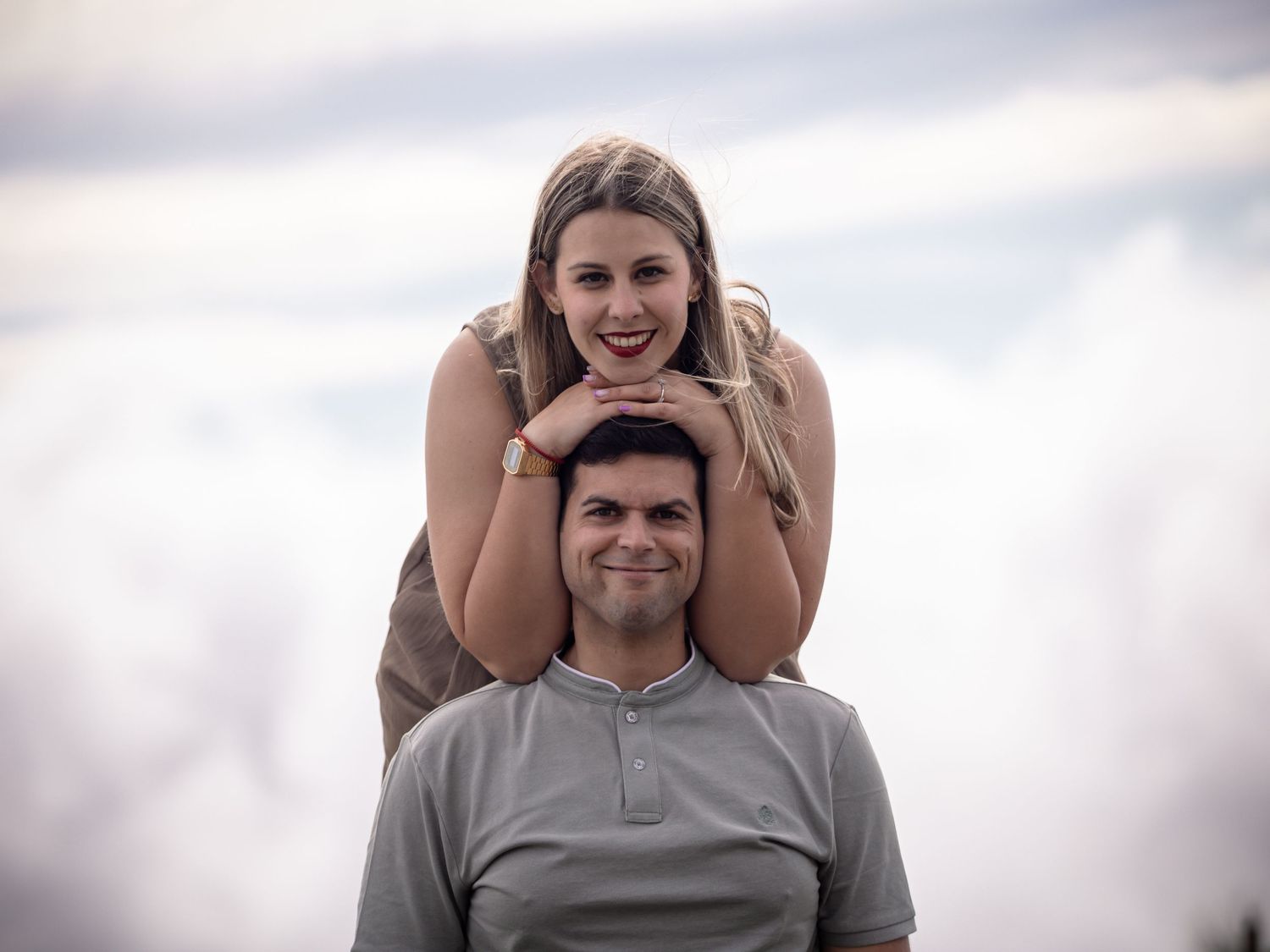 Playful outdoor couple photography session against cloudy sky.
