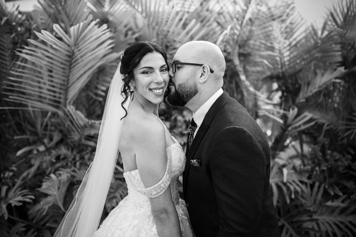 A black and white wedding portrait of a couple among tropical palm fronds.