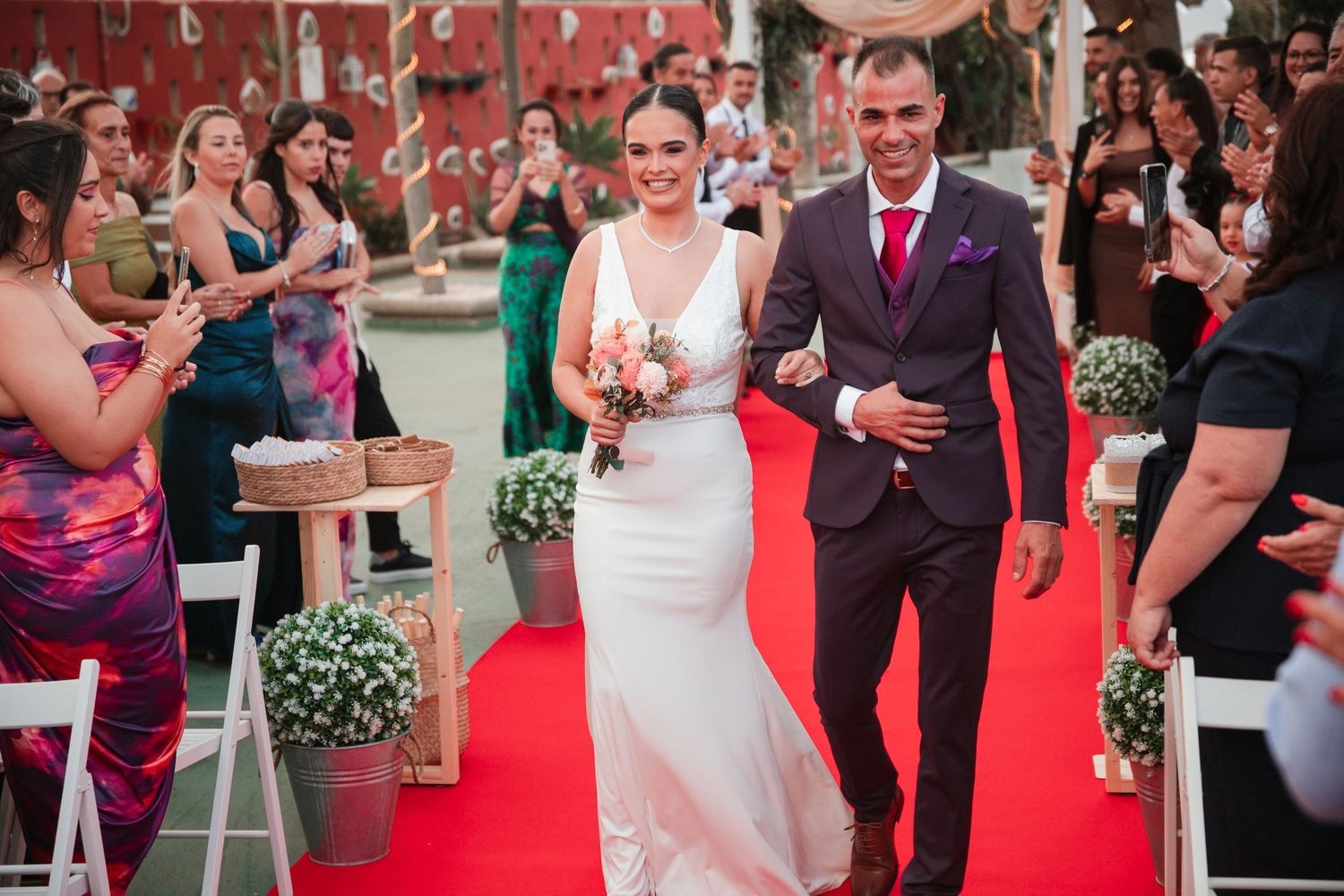 Wedding guests seated on a red carpet during an outdoor ceremony.