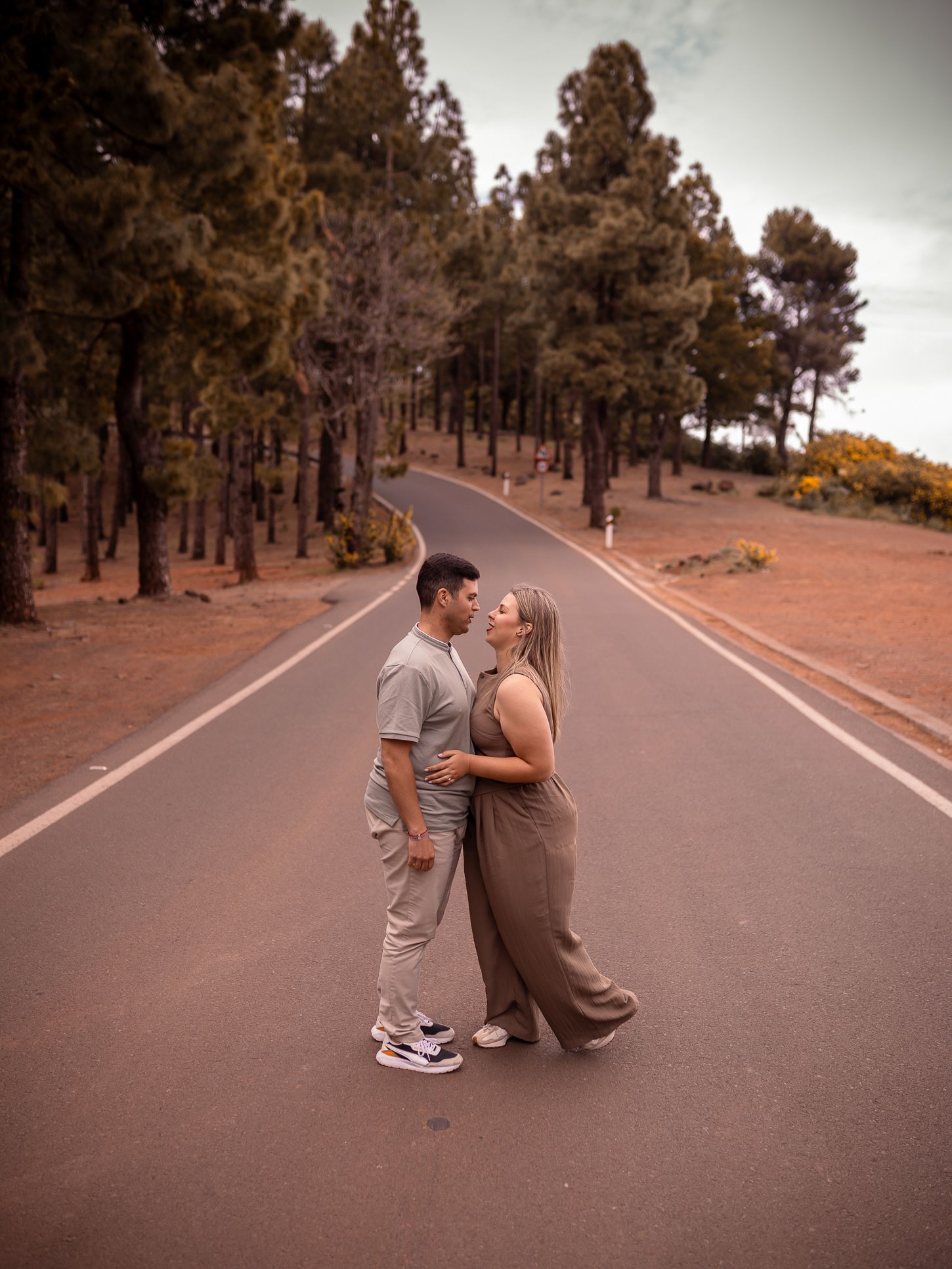 A playful couple dances and embraces on an empty mountain road at sunset.