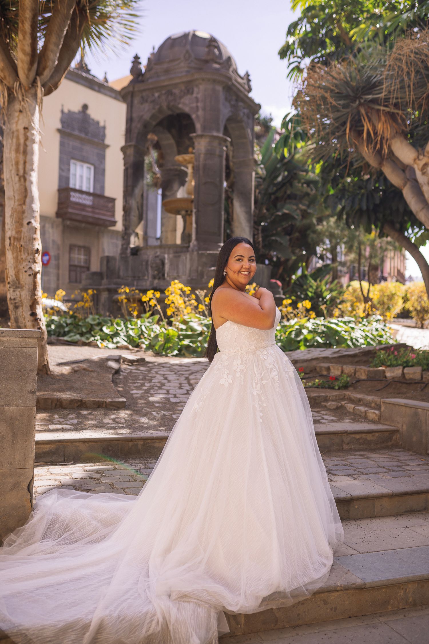 Flowing white wedding dress trails beautifully across stone courtyard with historic architecture.