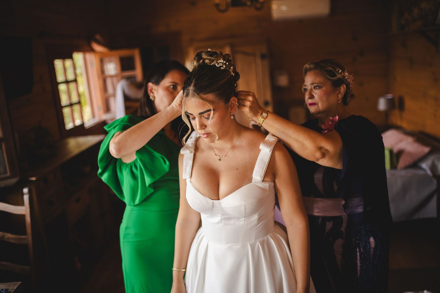 Wedding party members in green and white dresses prepare for the celebration in a rustic indoor setting.
