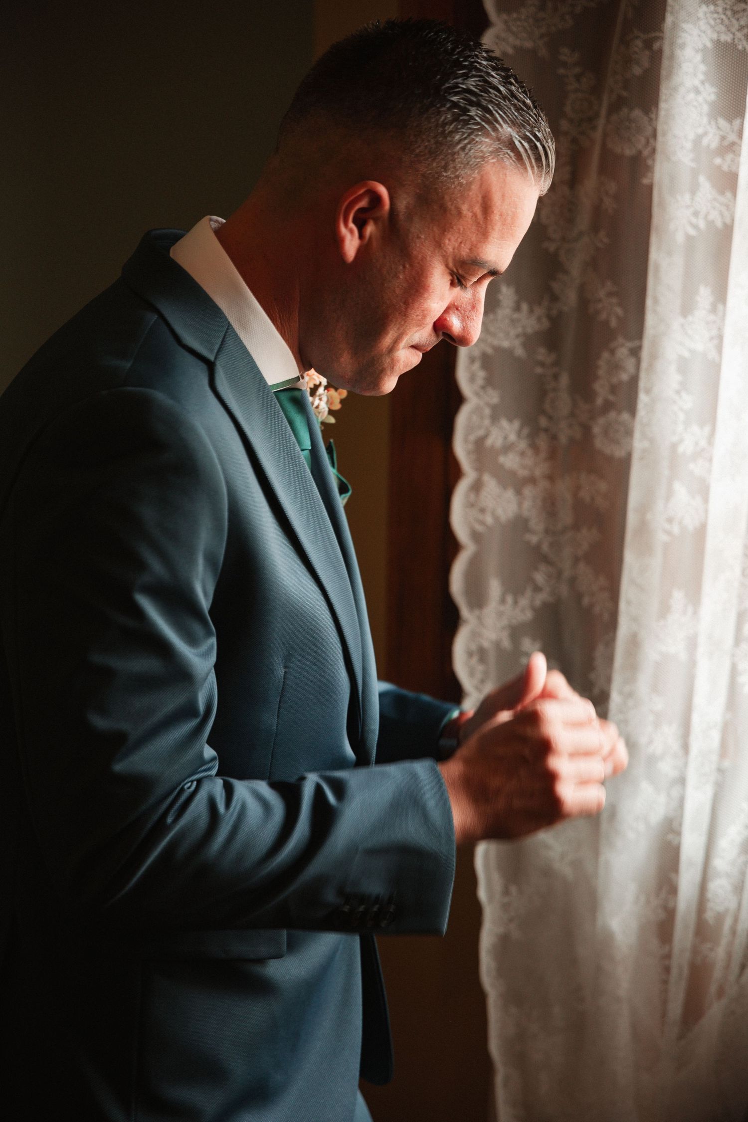 Dark suit photographed against lace curtains in dramatic lighting.