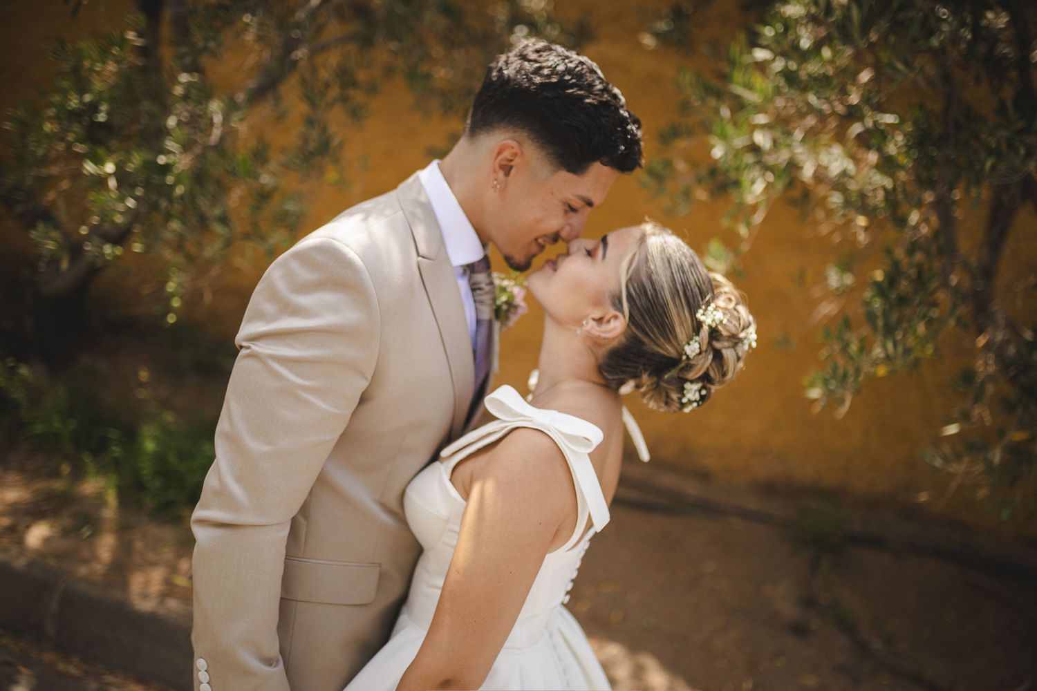 A romantic wedding couple shares an intimate moment against a rustic outdoor backdrop.