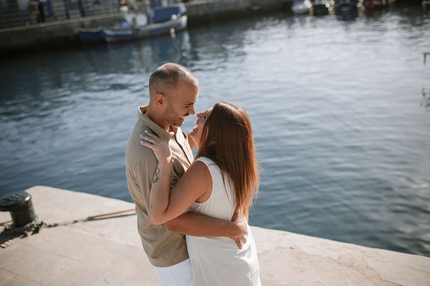 A couple embraces lovingly by the waterfront on a sunny afternoon.