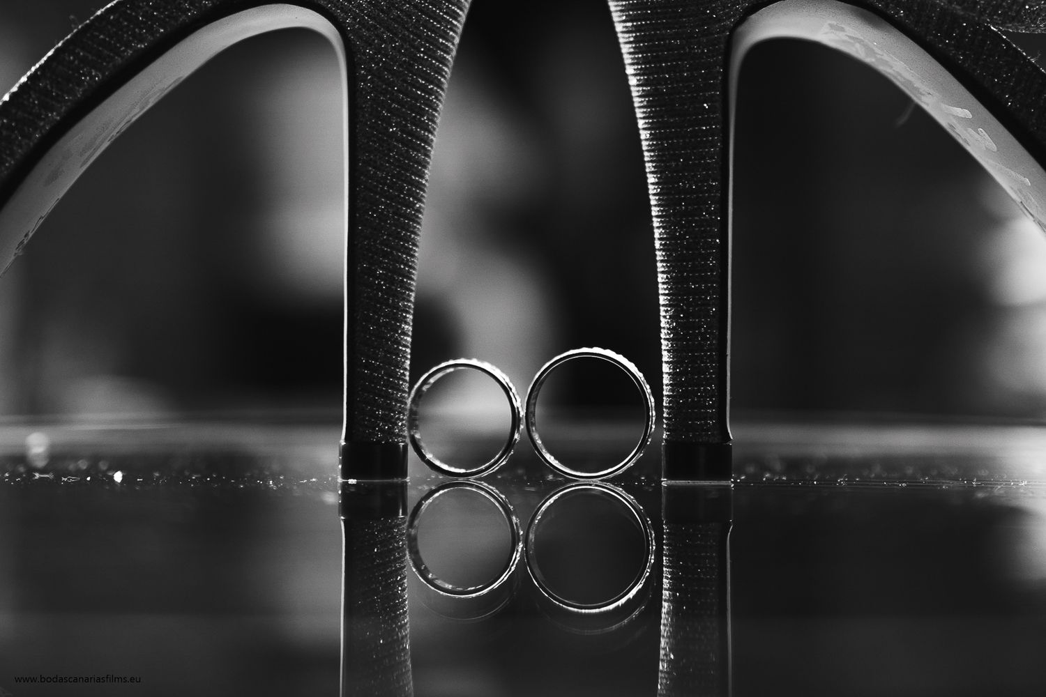 Wedding rings arranged artistically on black leather surface with dramatic lighting.