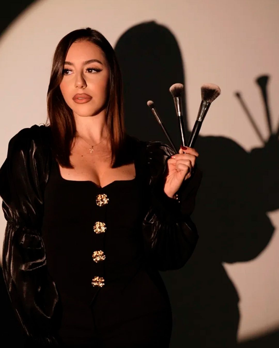 Dramatic portrait series showing figure in black against warm background with makeup brushes creating artistic shadows.