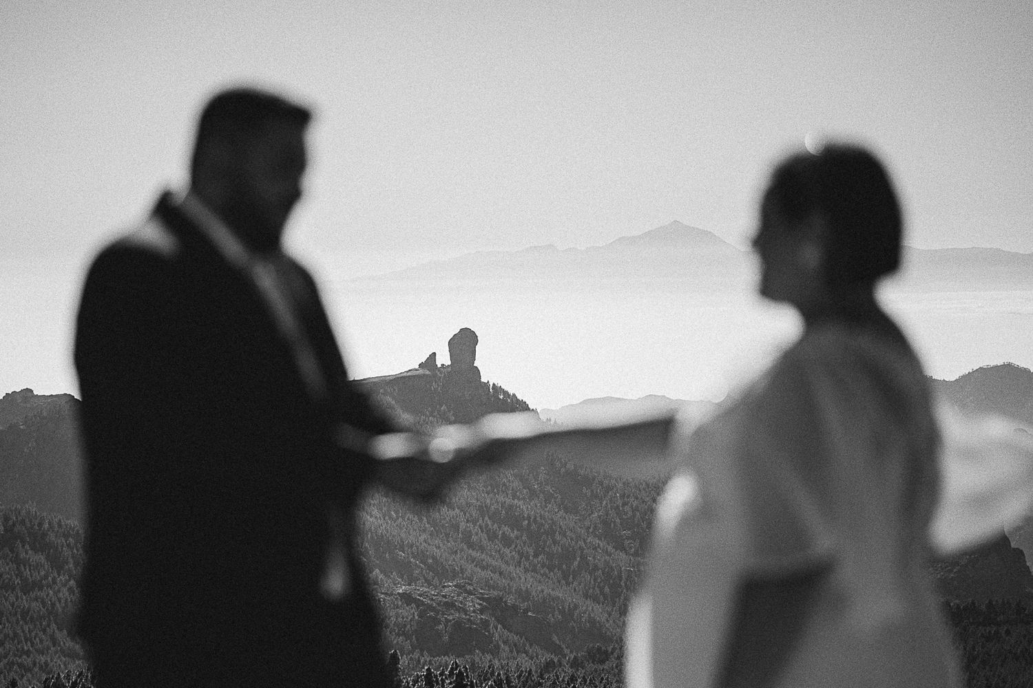 Black and white silhouette of a couple standing together with mountains in the background.