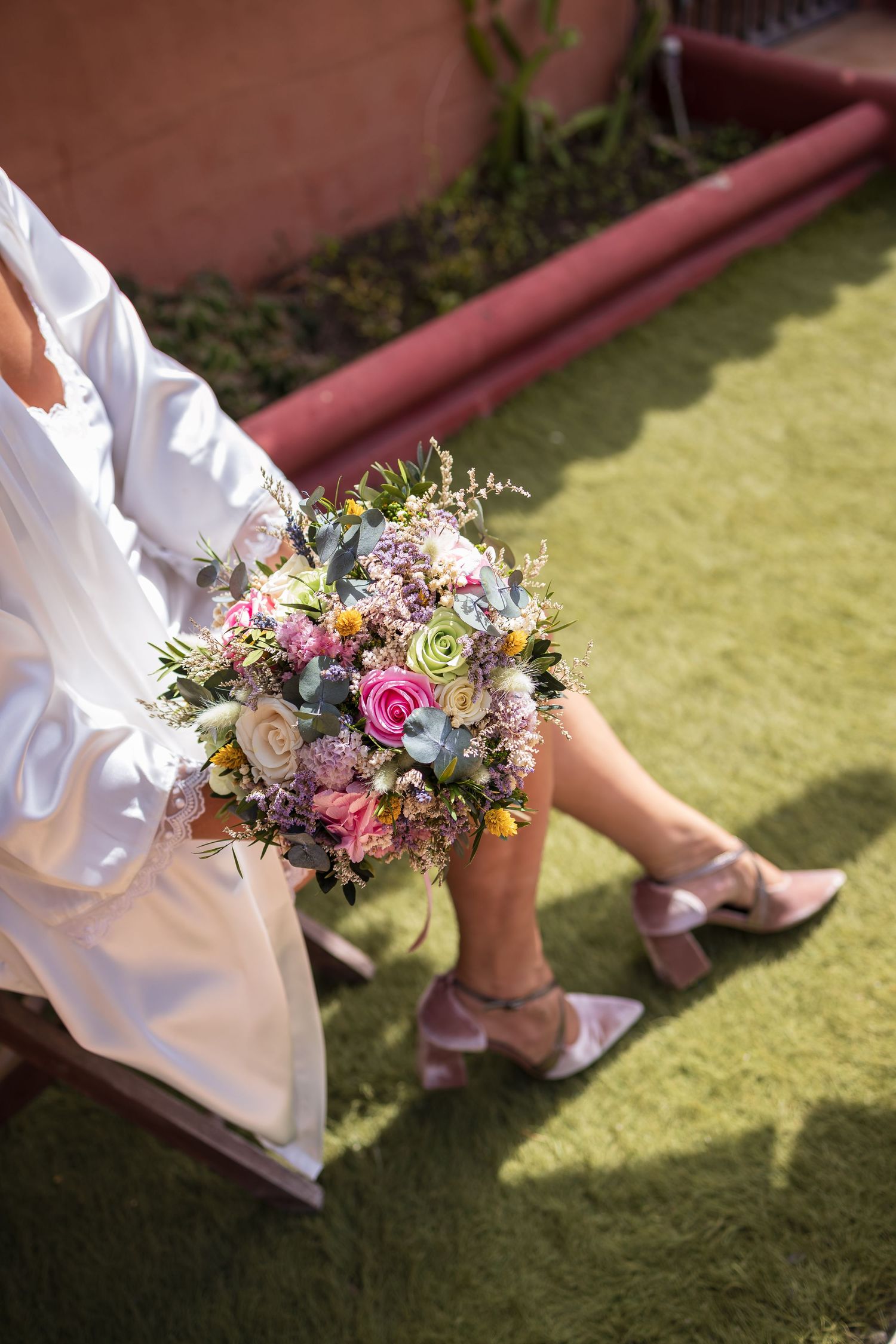 Delicate pink and white floral bouquet held against a white robe on grass.