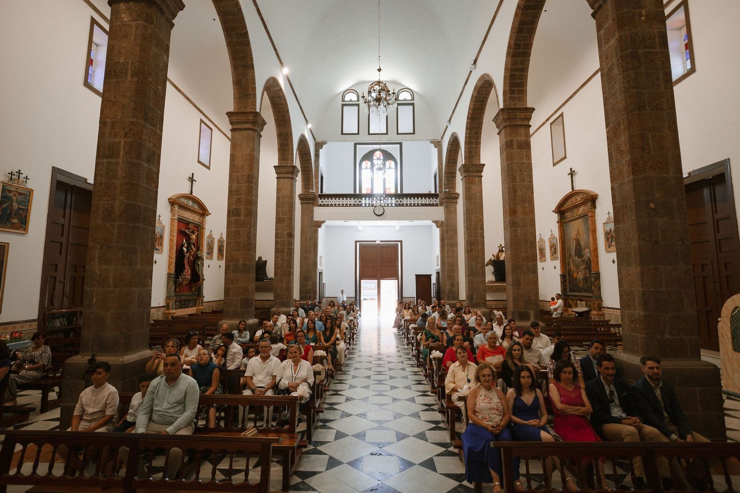 Interior of a grand cathedral with white columns and pews filled with wedding guests during a ceremony.