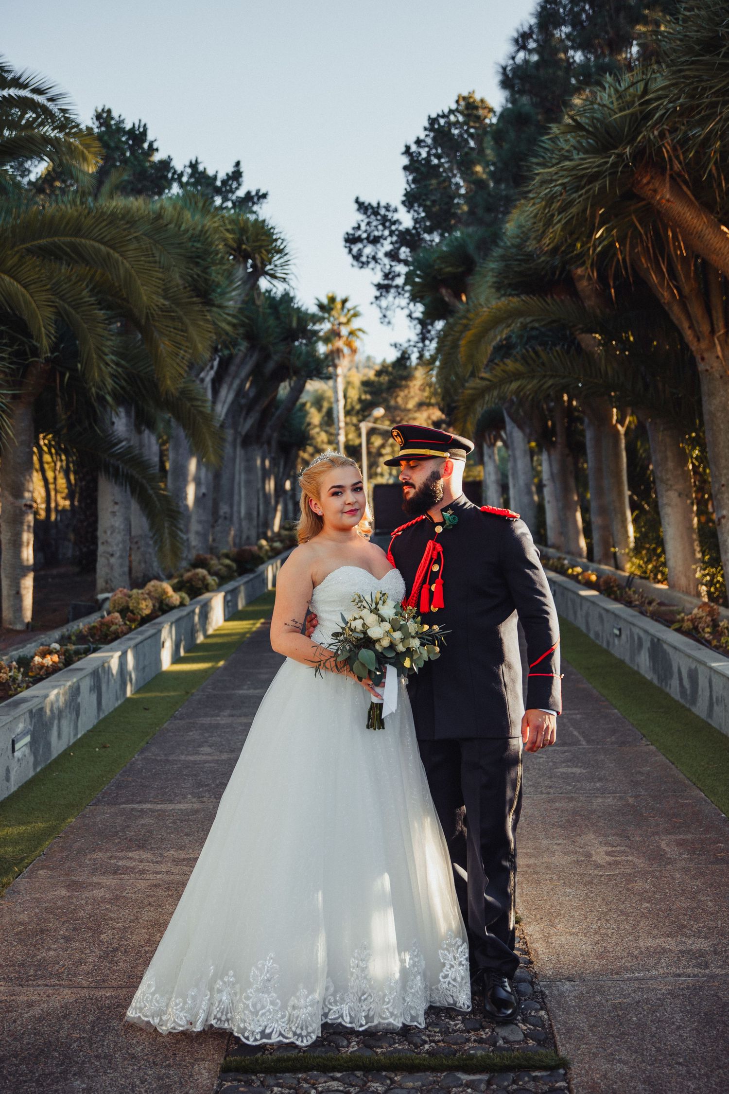 A bride and groom share intimate moments along a palm tree-lined pathway at their wedding.
