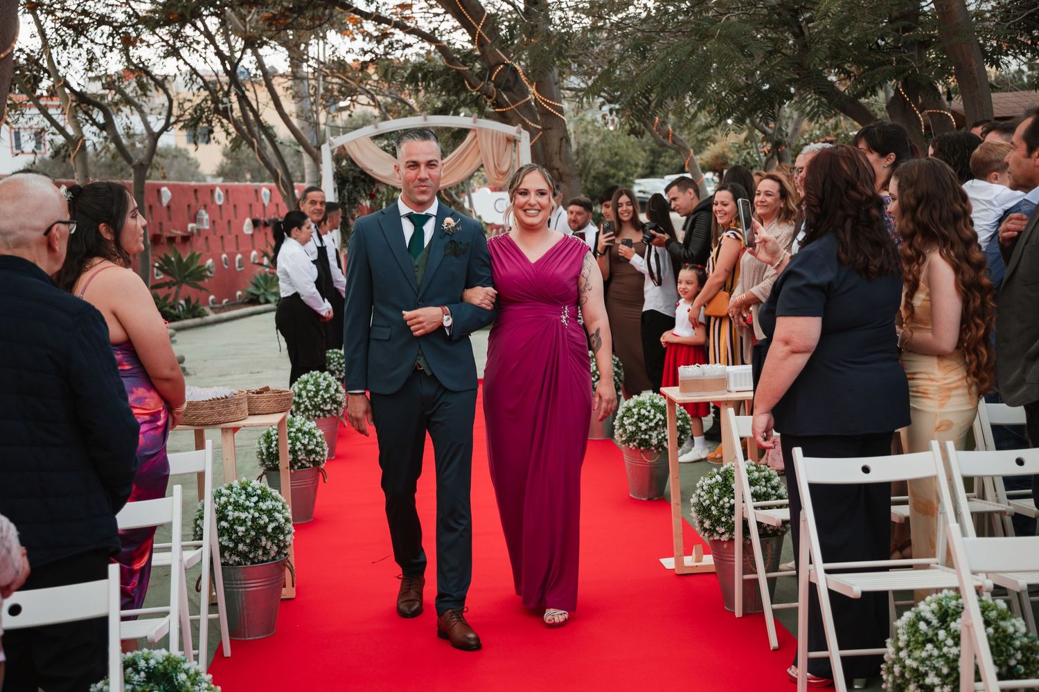 Outdoor wedding ceremony setup with white chairs and red carpet aisle runner.