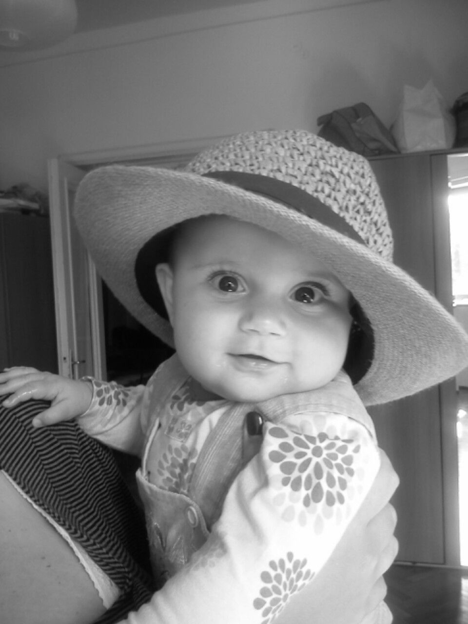 A baby wearing a white sun hat and floral bib in black and white photography.