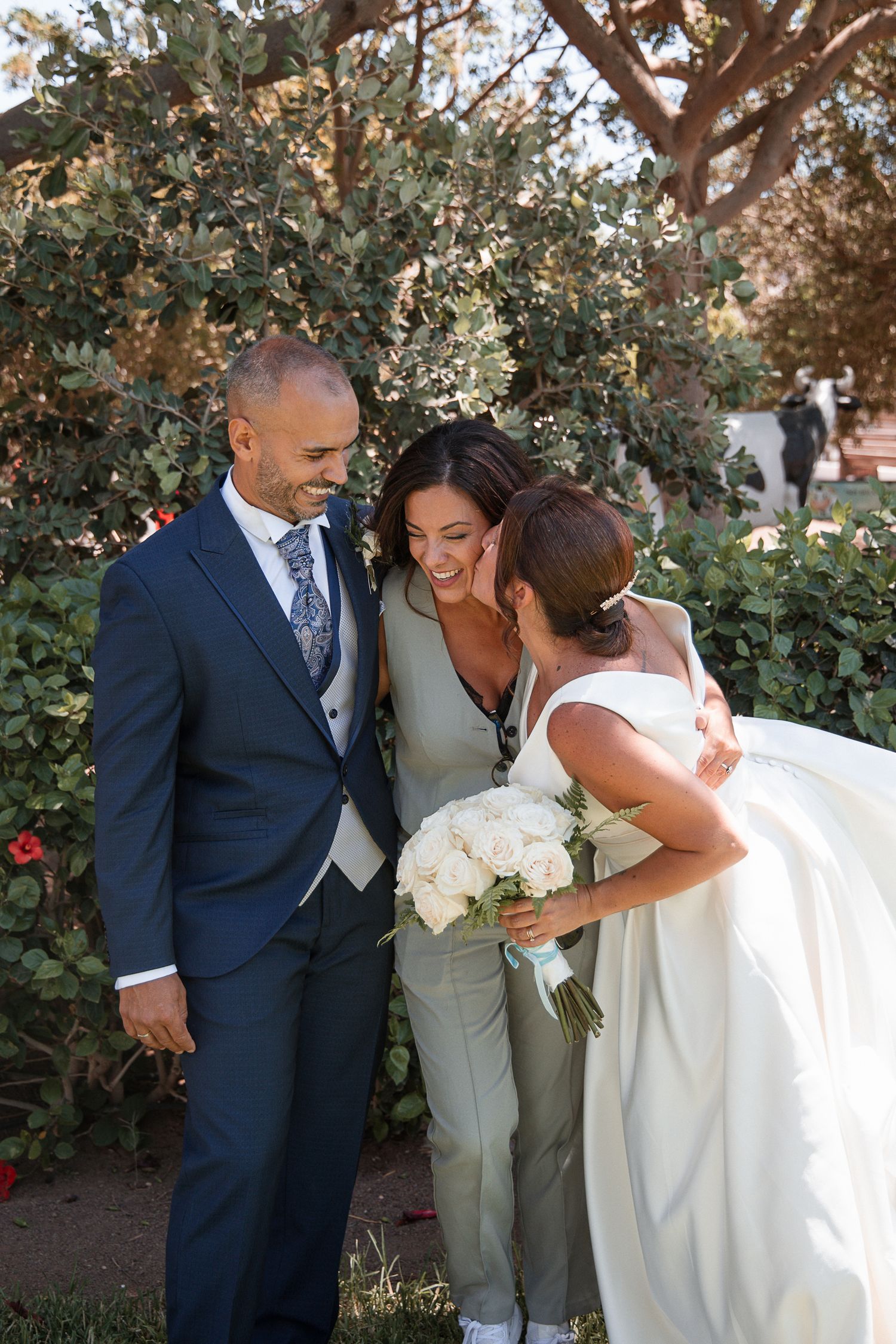 Wedding couple shares intimate moments in a garden setting with white floral bouquet and formal attire.