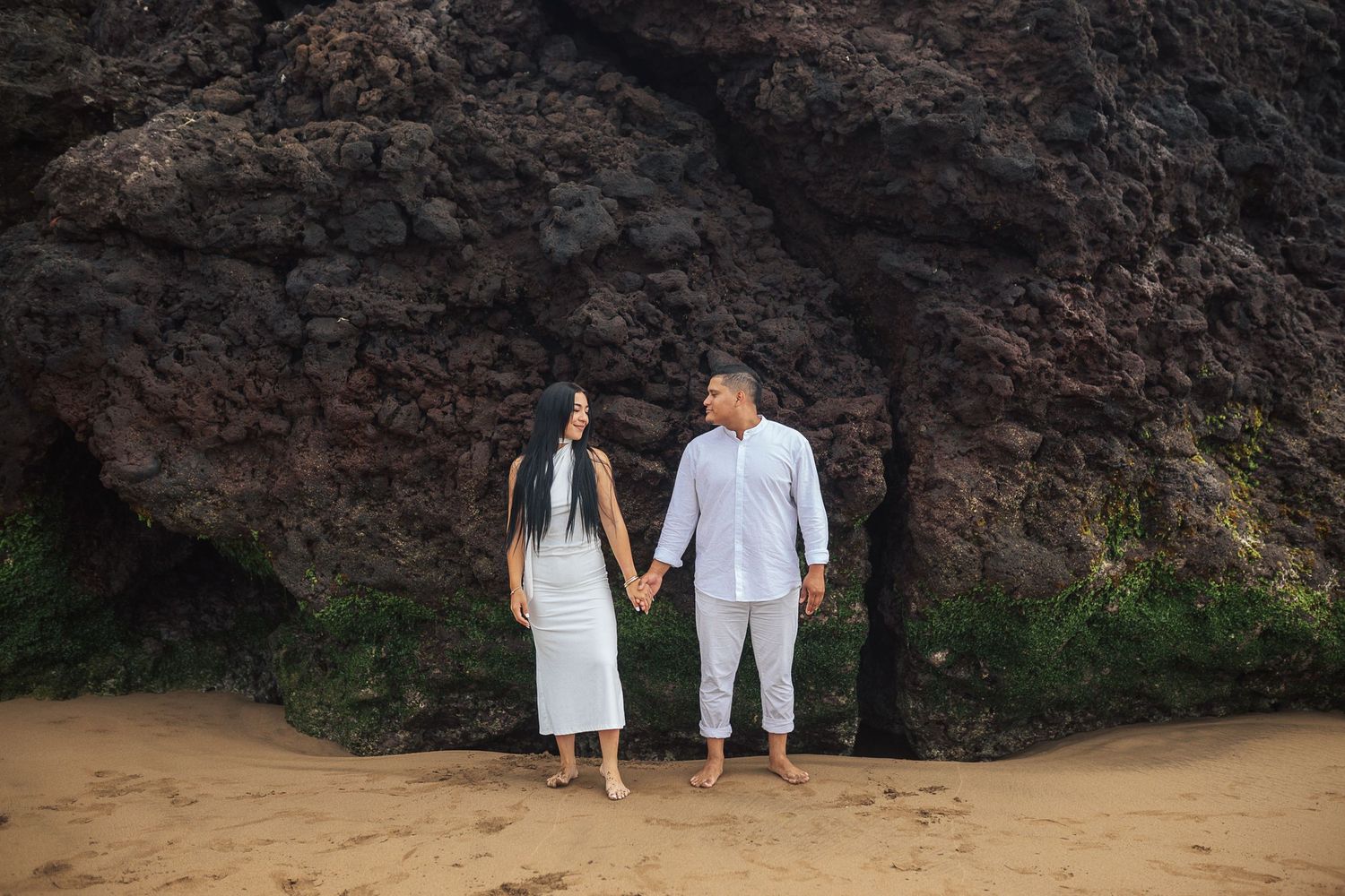 Couple holding hands while walking along a rocky beach at sunset.